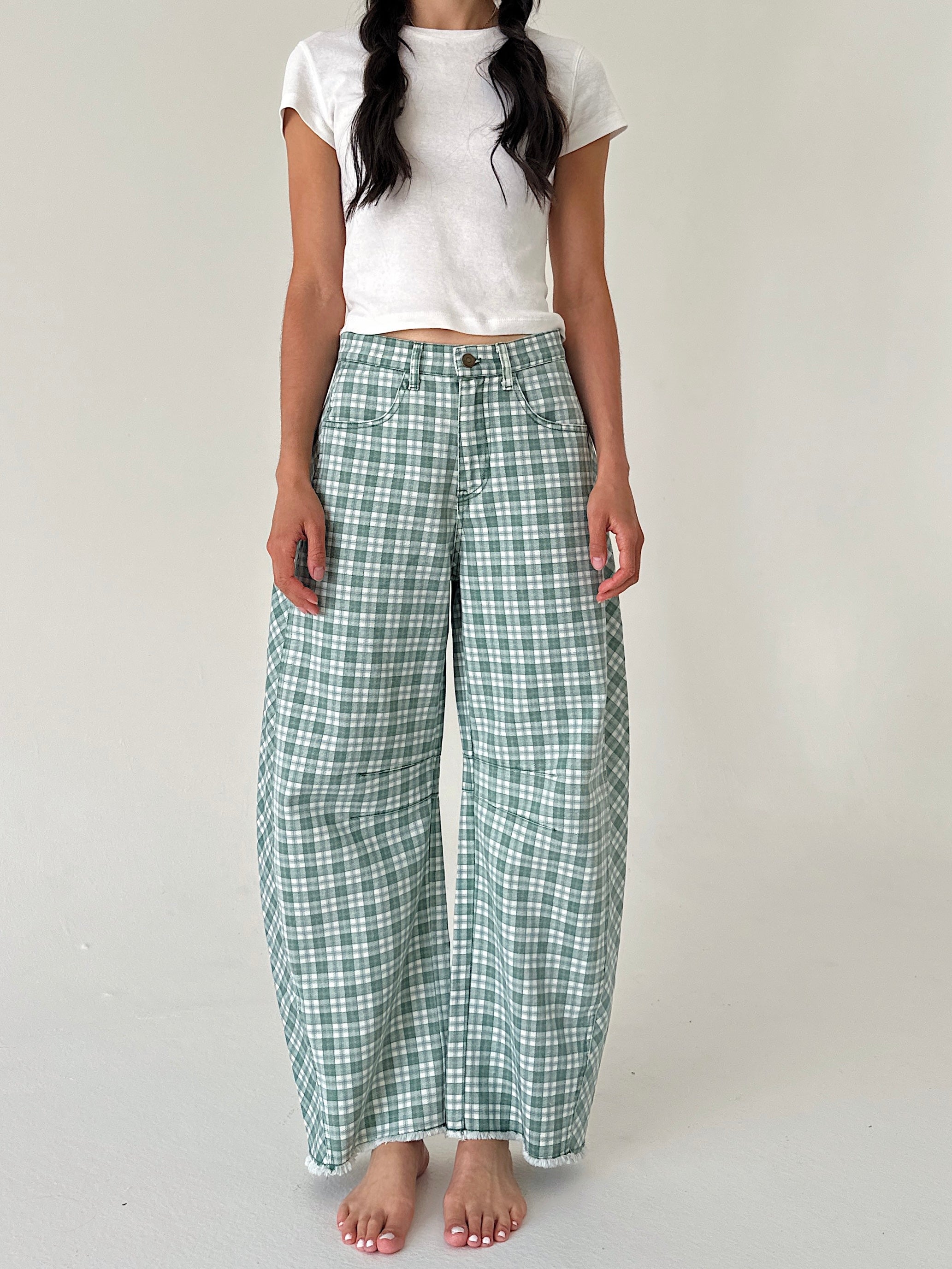 A model wearing green and white plaid wide-leg pants with a white cropped t-shirt, standing against a plain light gray studio background.