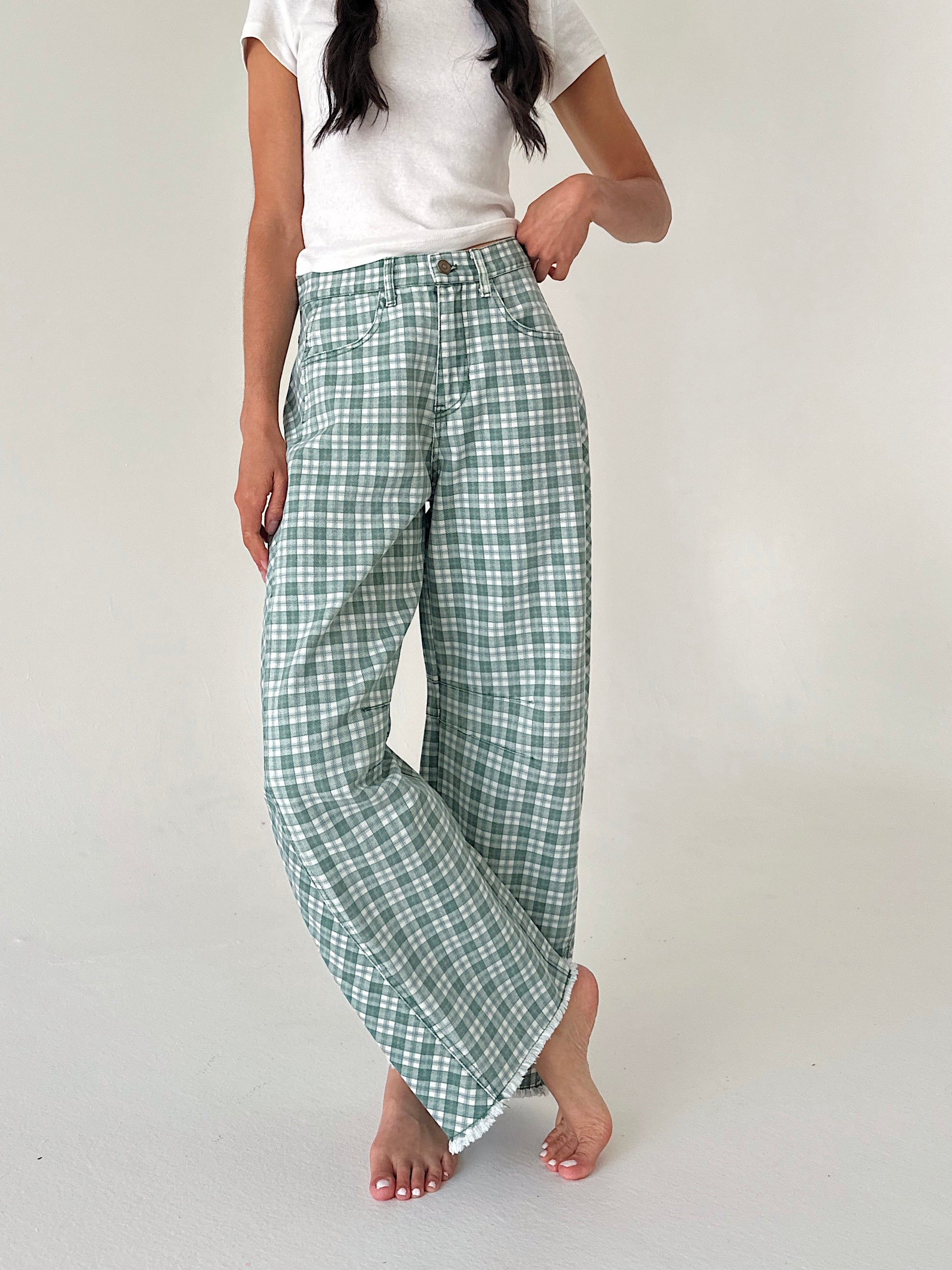 A person modeling a pair of wide-leg pants with a green and white plaid pattern, paired with a white t-shirt, against a plain light gray studio background.