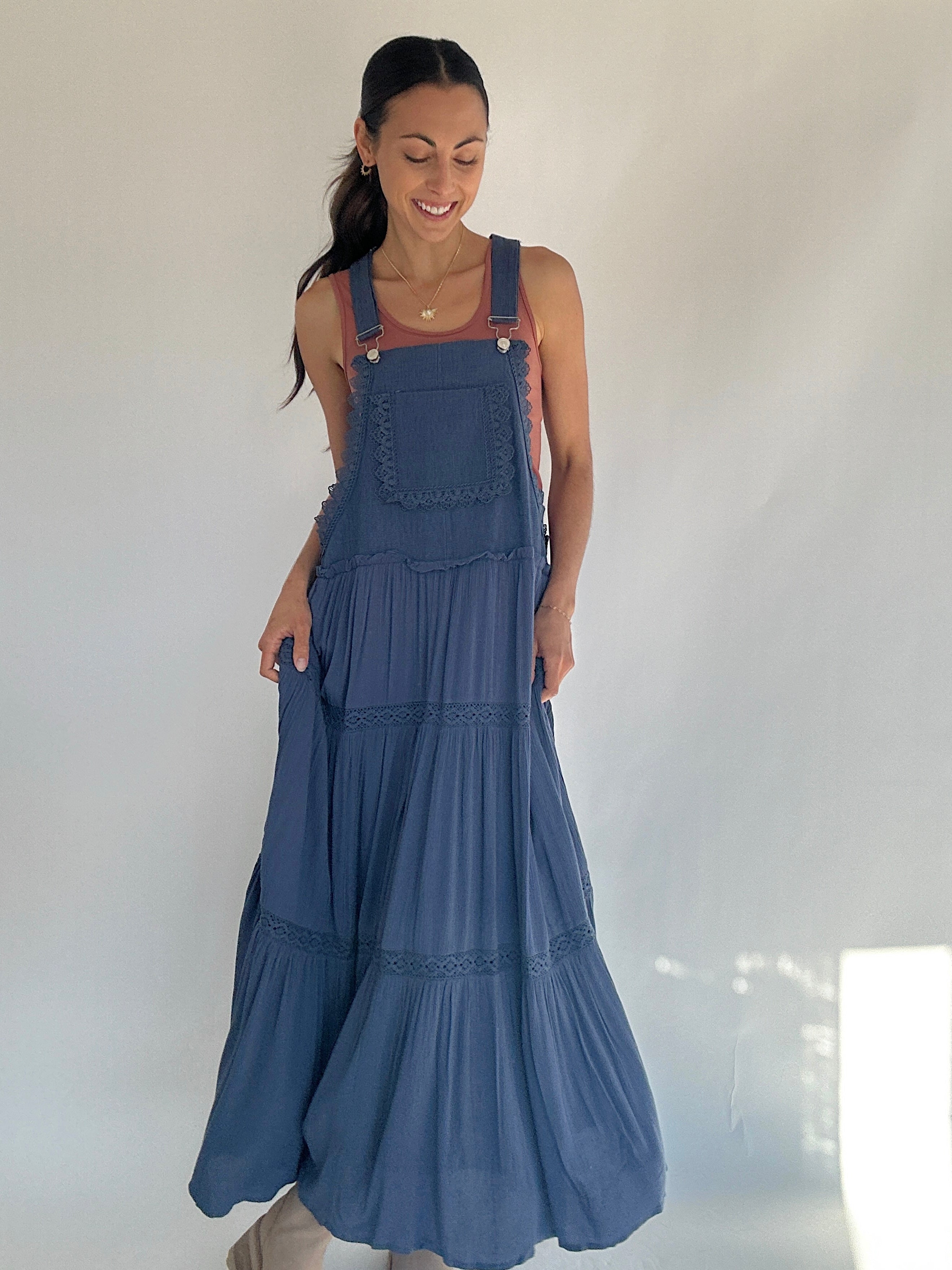 Woman wearing a blue denim overall dress against a plain background