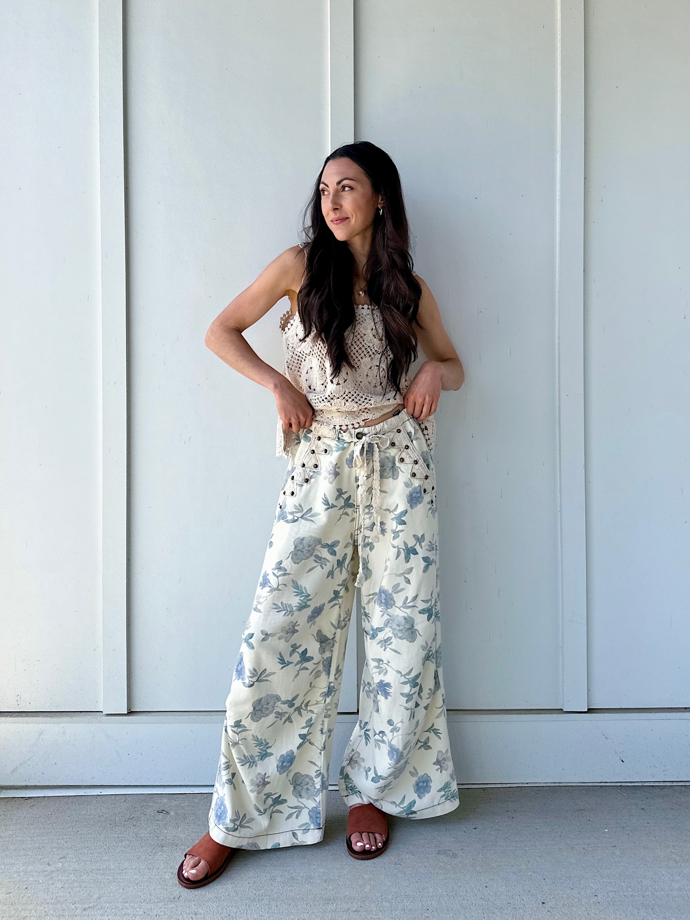 Woman wearing cream and blue floral pants standing against a white wall.