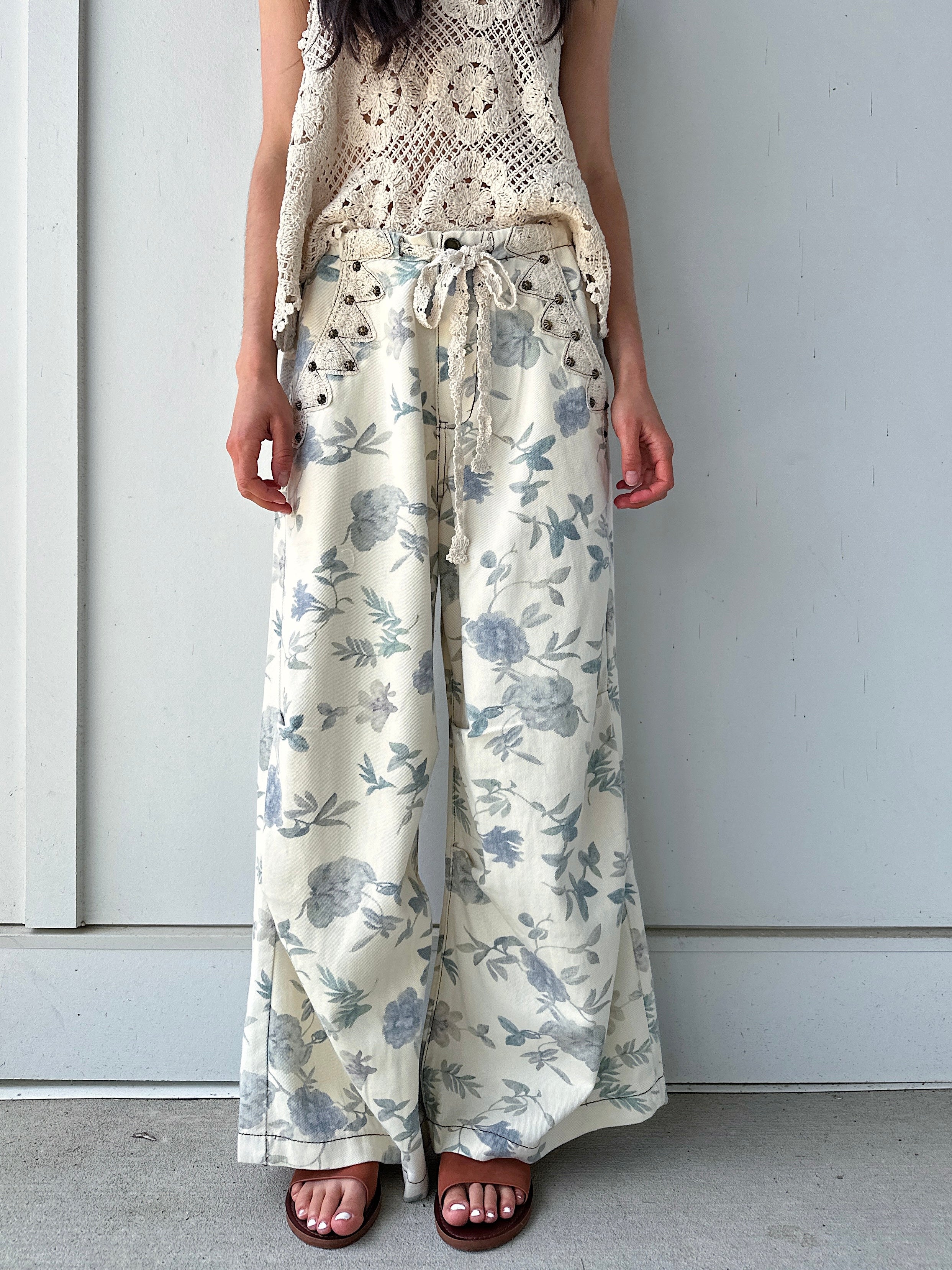 Person wearing cream and white floral wide-leg pants against a plain background