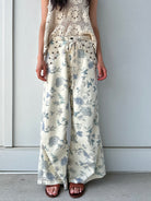Person wearing cream and white floral wide-leg pants against a plain background
