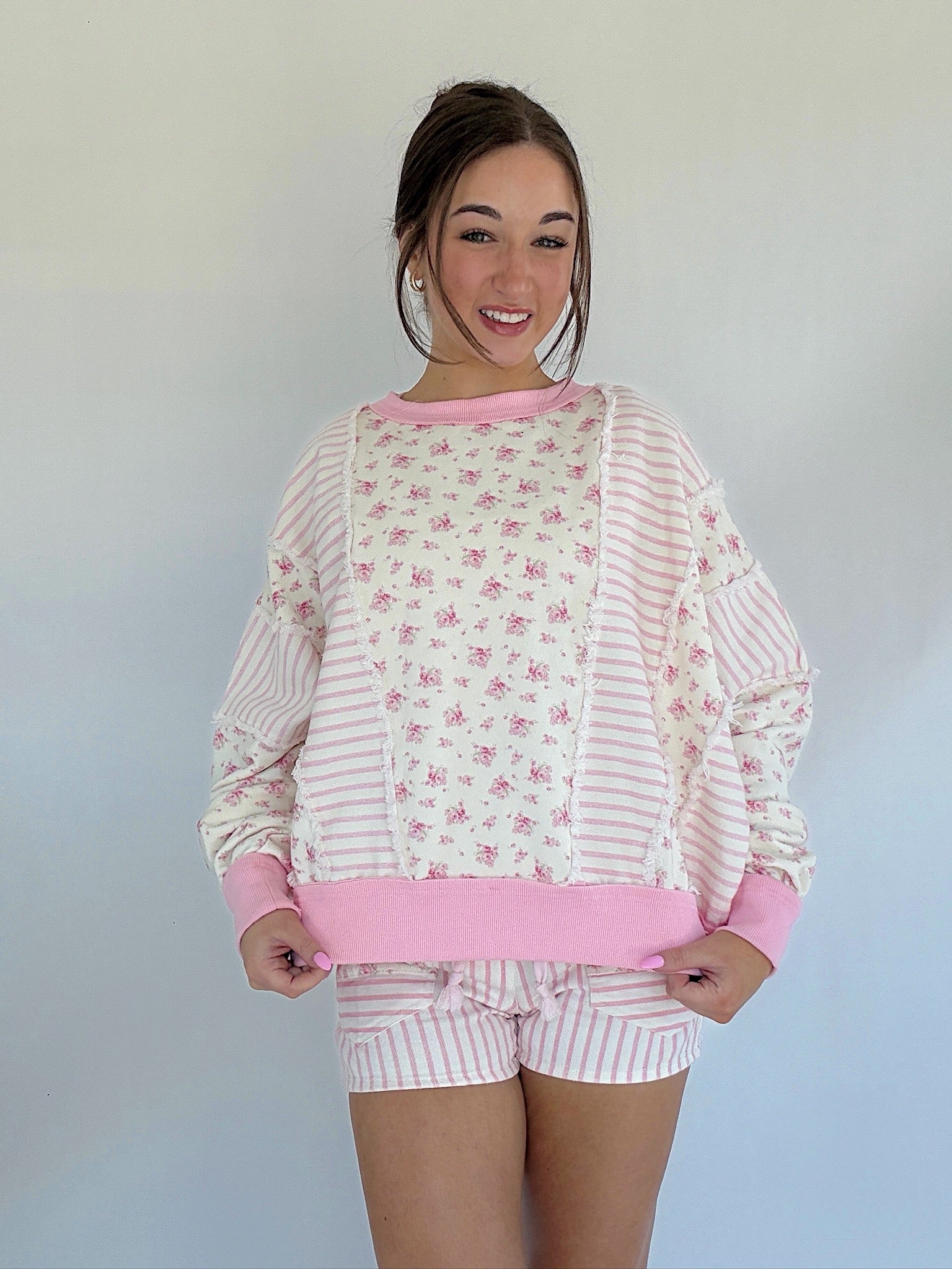Woman wearing a pink and white pullover top with a floral pattern against a plain background
