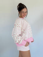 Woman wearing a pink and white striped outfit with floral details against a plain background