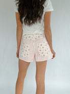 Person wearing a white t-shirt and floral shorts on a plain background from back