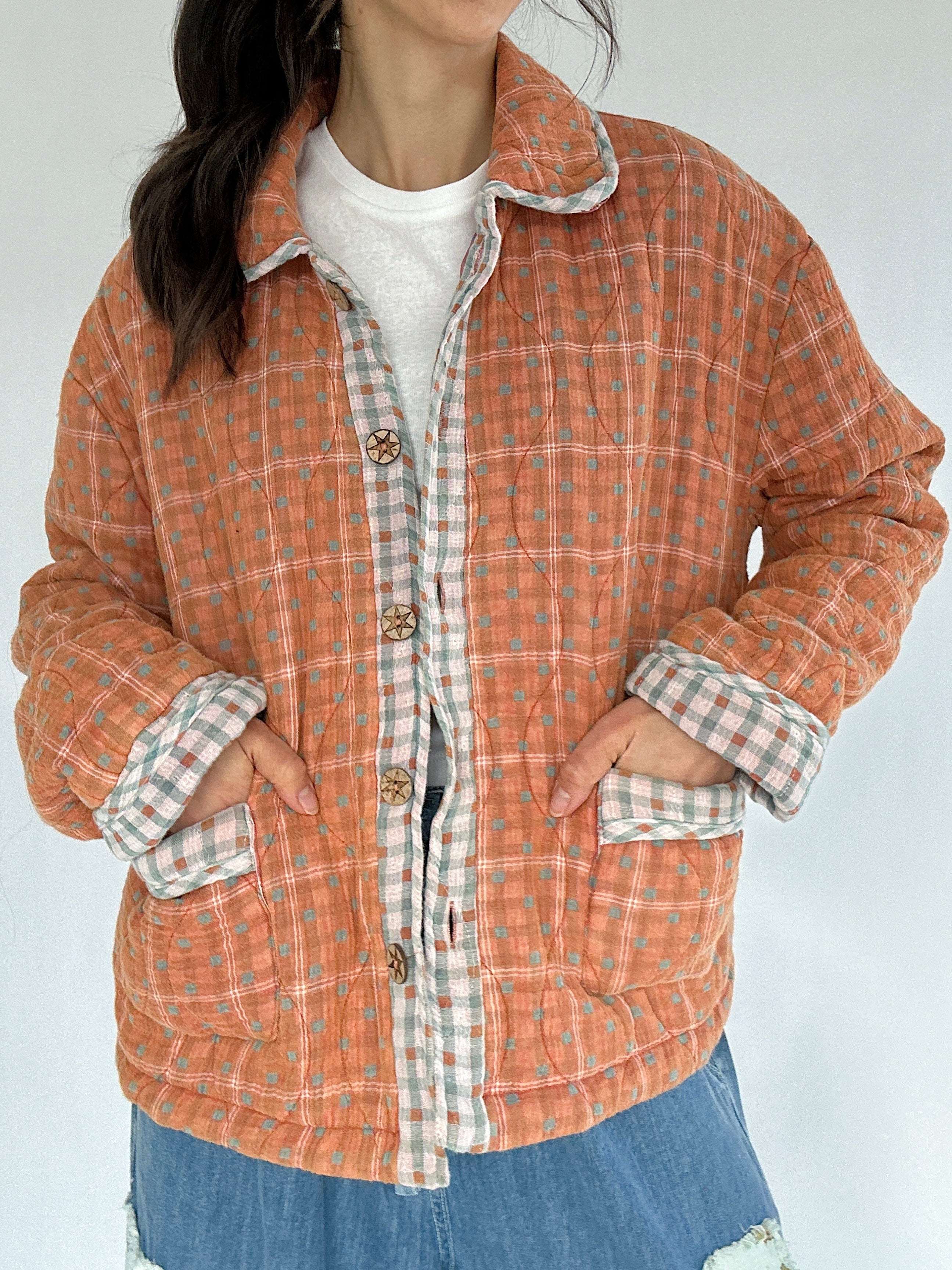 Person wearing a rust orange plaid jacket that has contrast trim and wood buttons with a white background