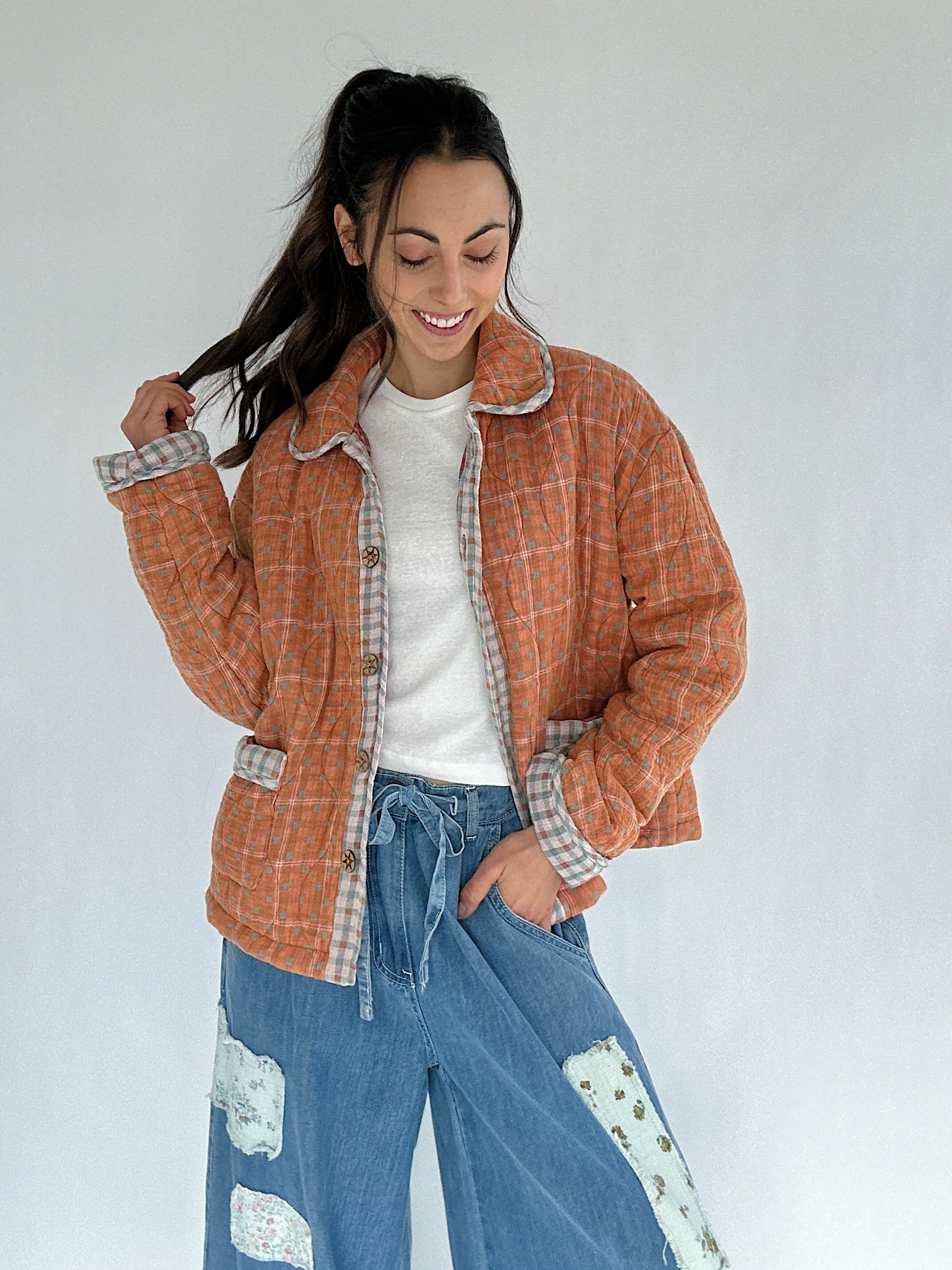 Woman wearing a rust orange plaid jacket and blue jeans against a white background