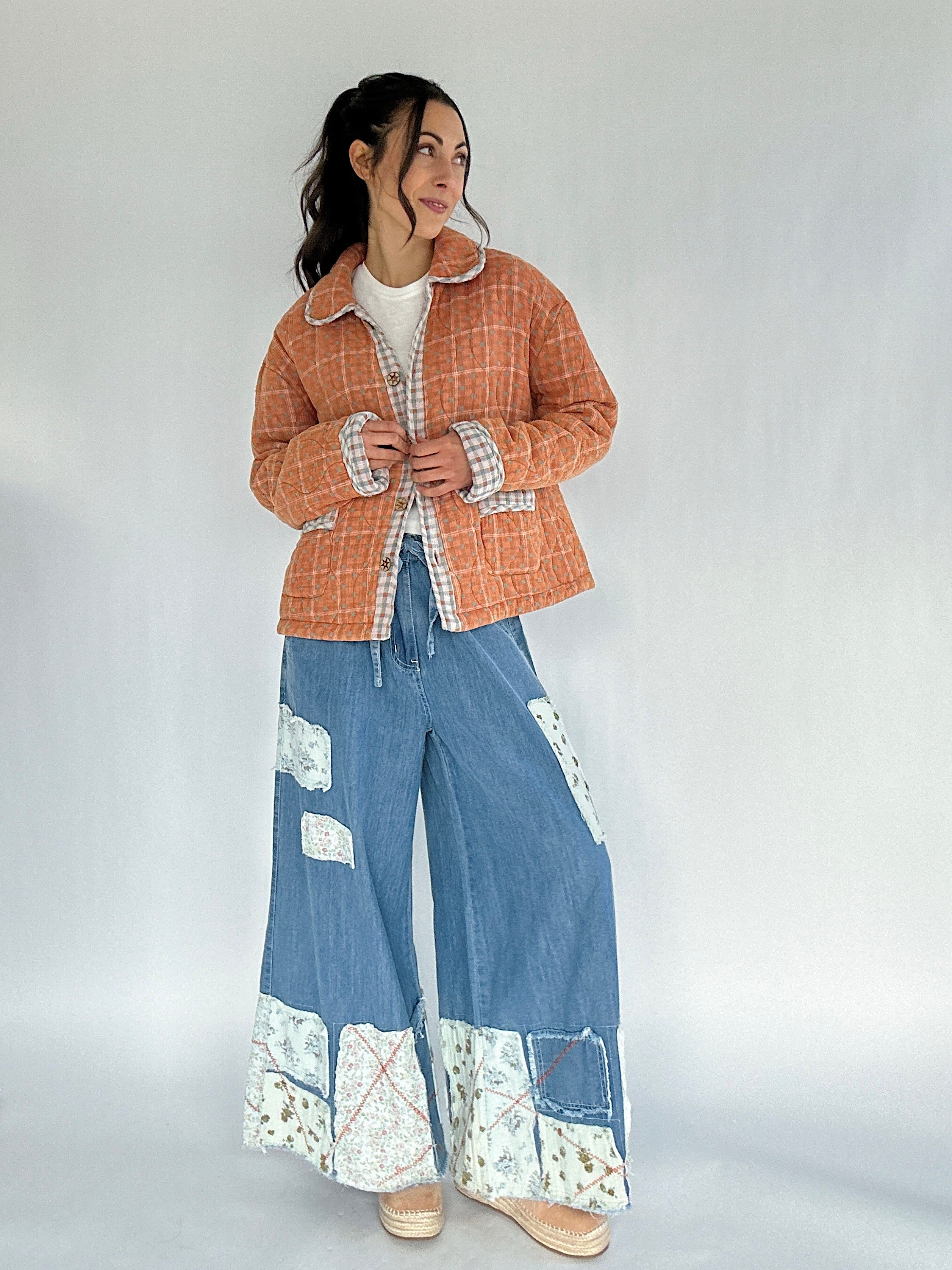 Person wearing a checkered jacket and blue denim pants with floral patterns on a plain background