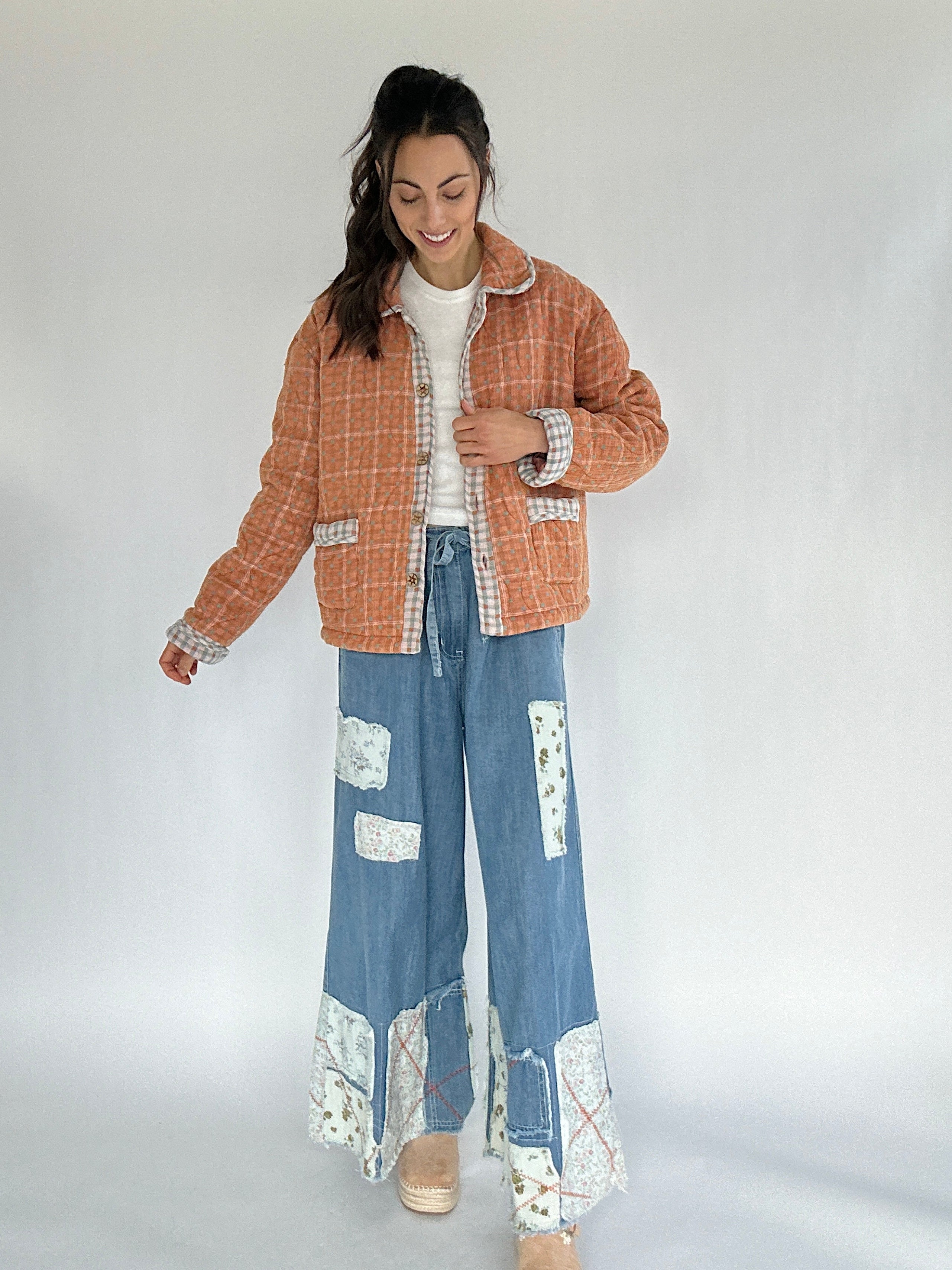 Woman wearing a checkered jacket and denim pants with floral patterns on a white background