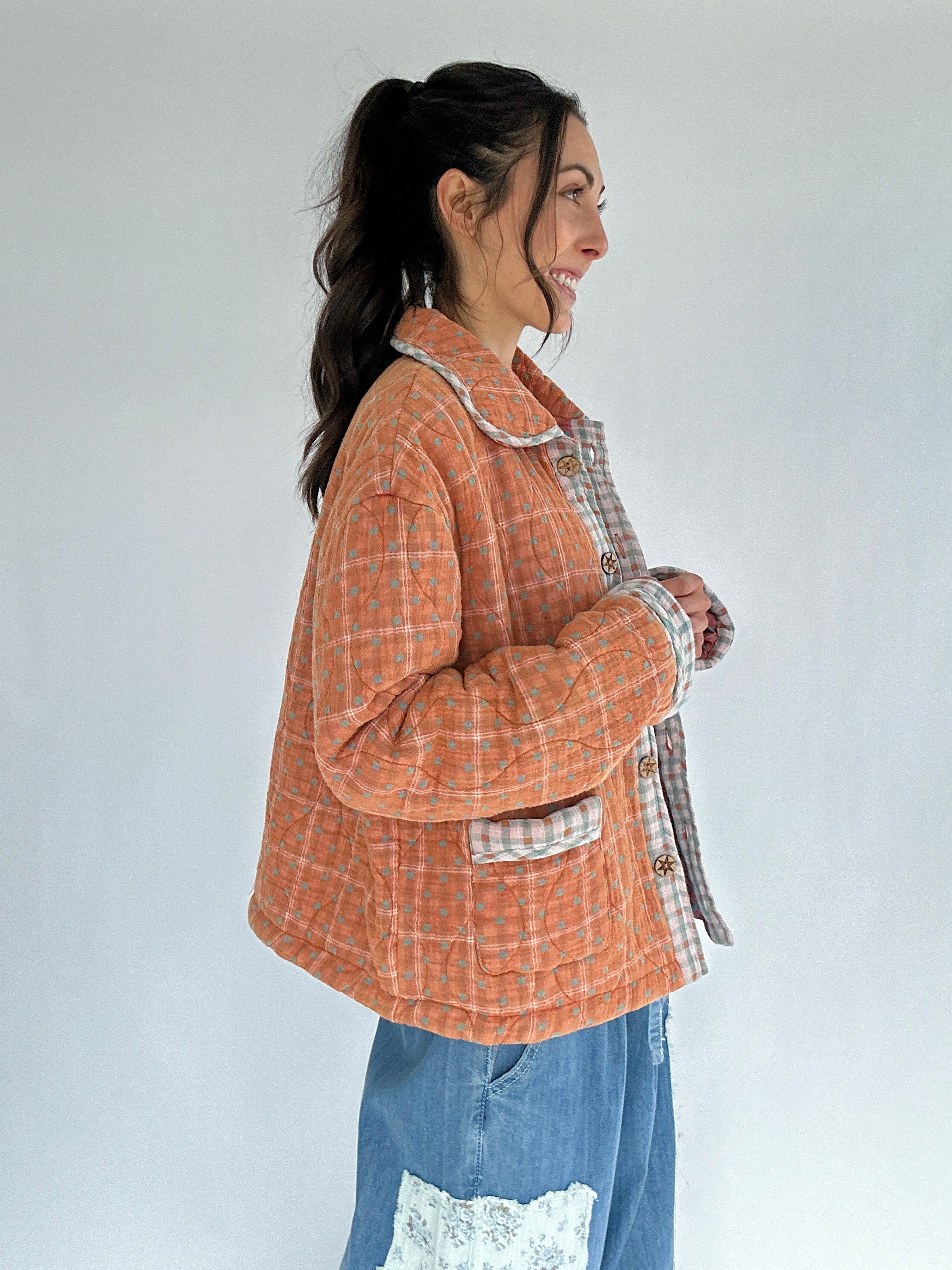 Woman wearing a checkered jacket over a plaid shirt with a white background from side