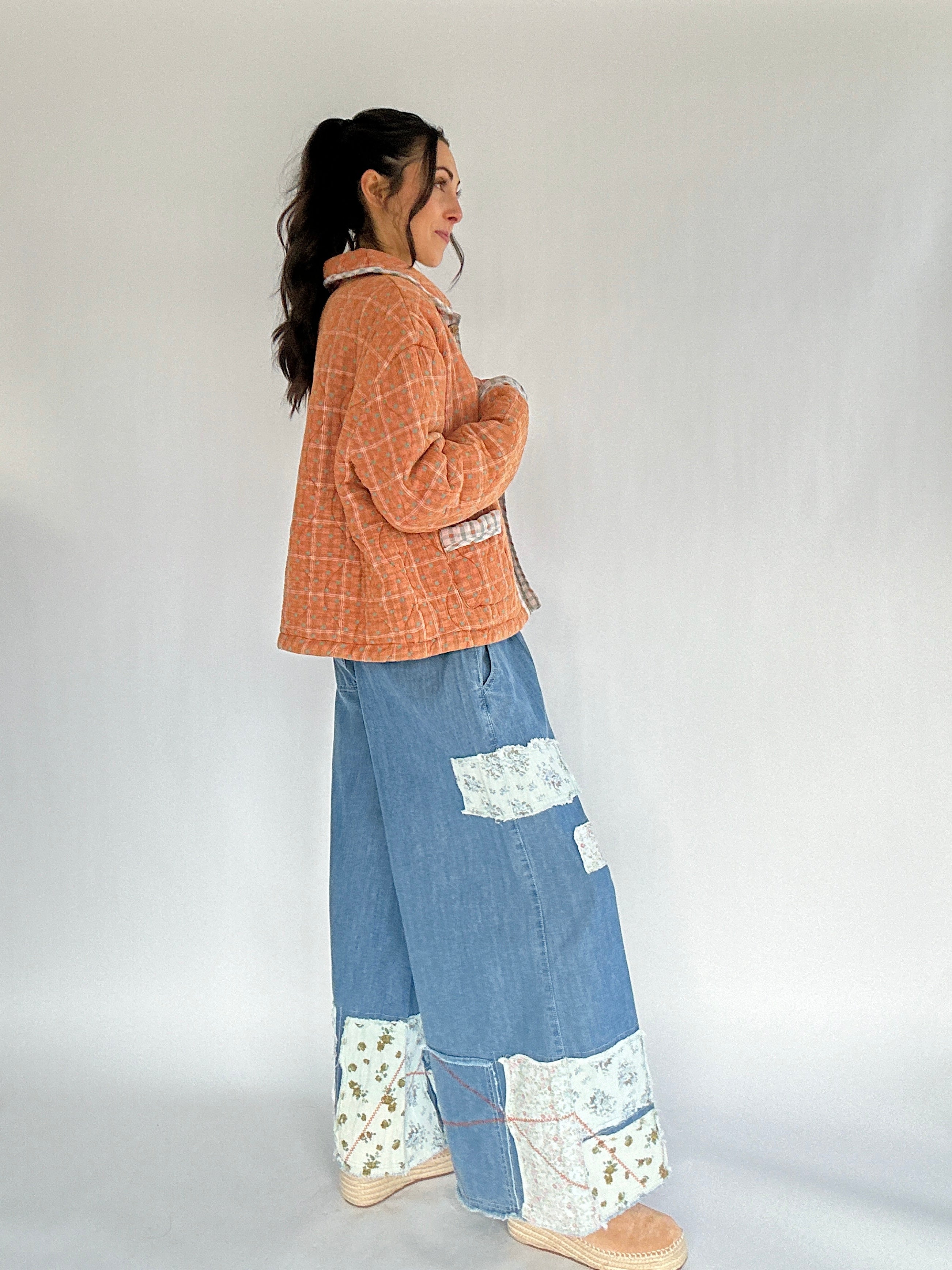 Person wearing a rust orange plaid jacket and blue patchwork pants on a white background