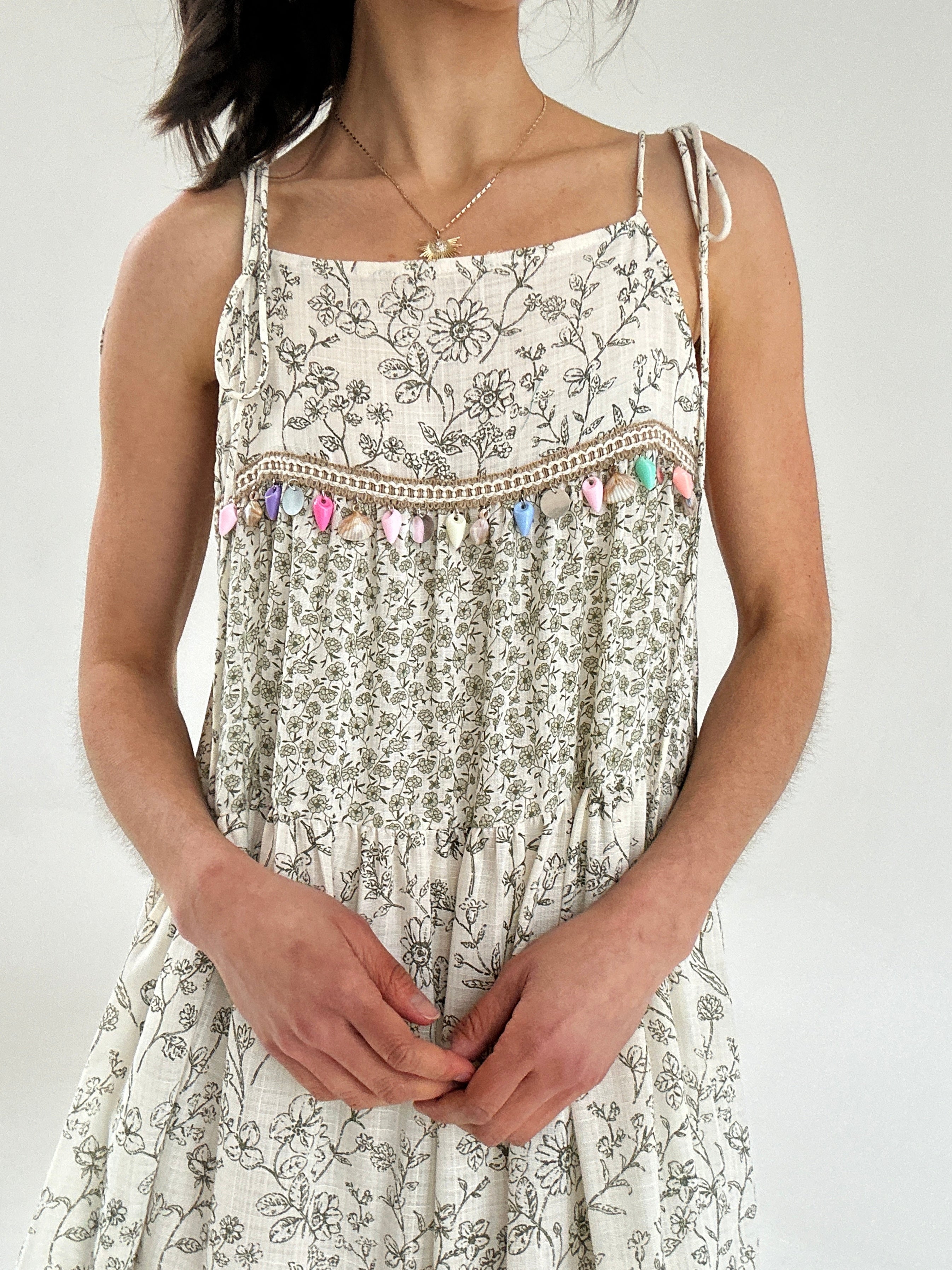 Woman wearing a floral dress with decorative straps against a white background