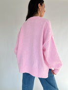 Person wearing a pink sweater and blue jeans against a plain background