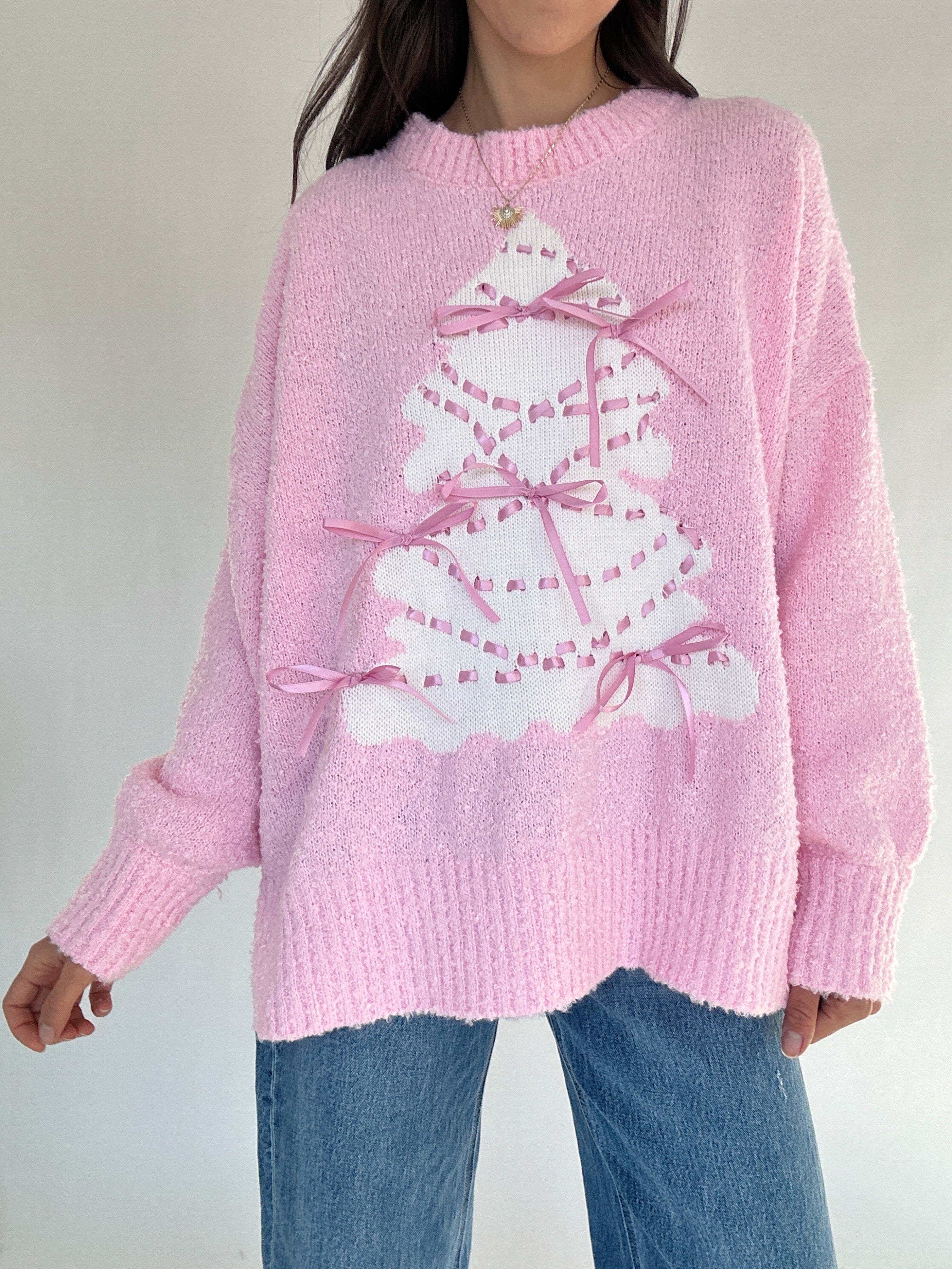 Person wearing a pink sweater with a white tree design on a plain background