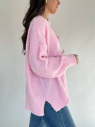 Person wearing a pink knitted sweater and blue jeans against a plain background from side