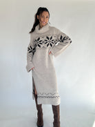Woman wearing a long, patterned sweater dress with cowl neck against a white background