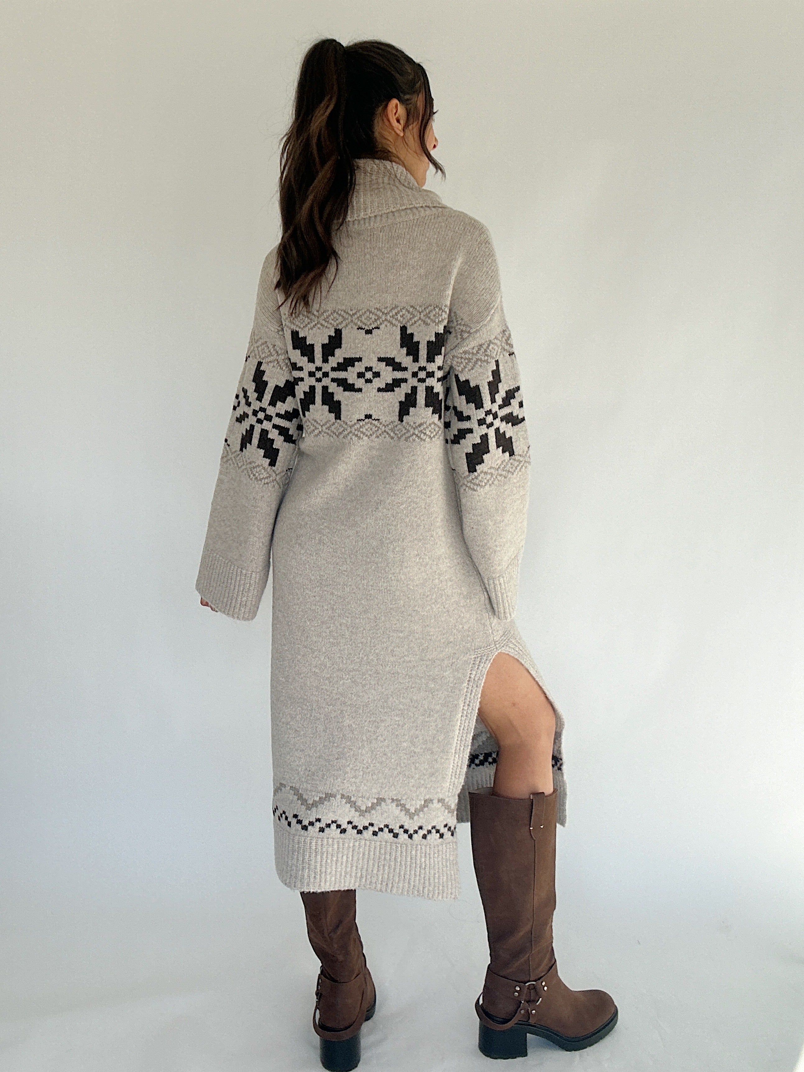 Person wearing a long beige sweater with black pattern on a white background showing back