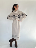 Woman wearing a long beige sweater with a pattern, standing against a white background
