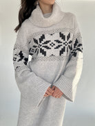 Person wearing a gray sweater dress with a black and white winter pattern and cowl neckline on a plain background showing top detail