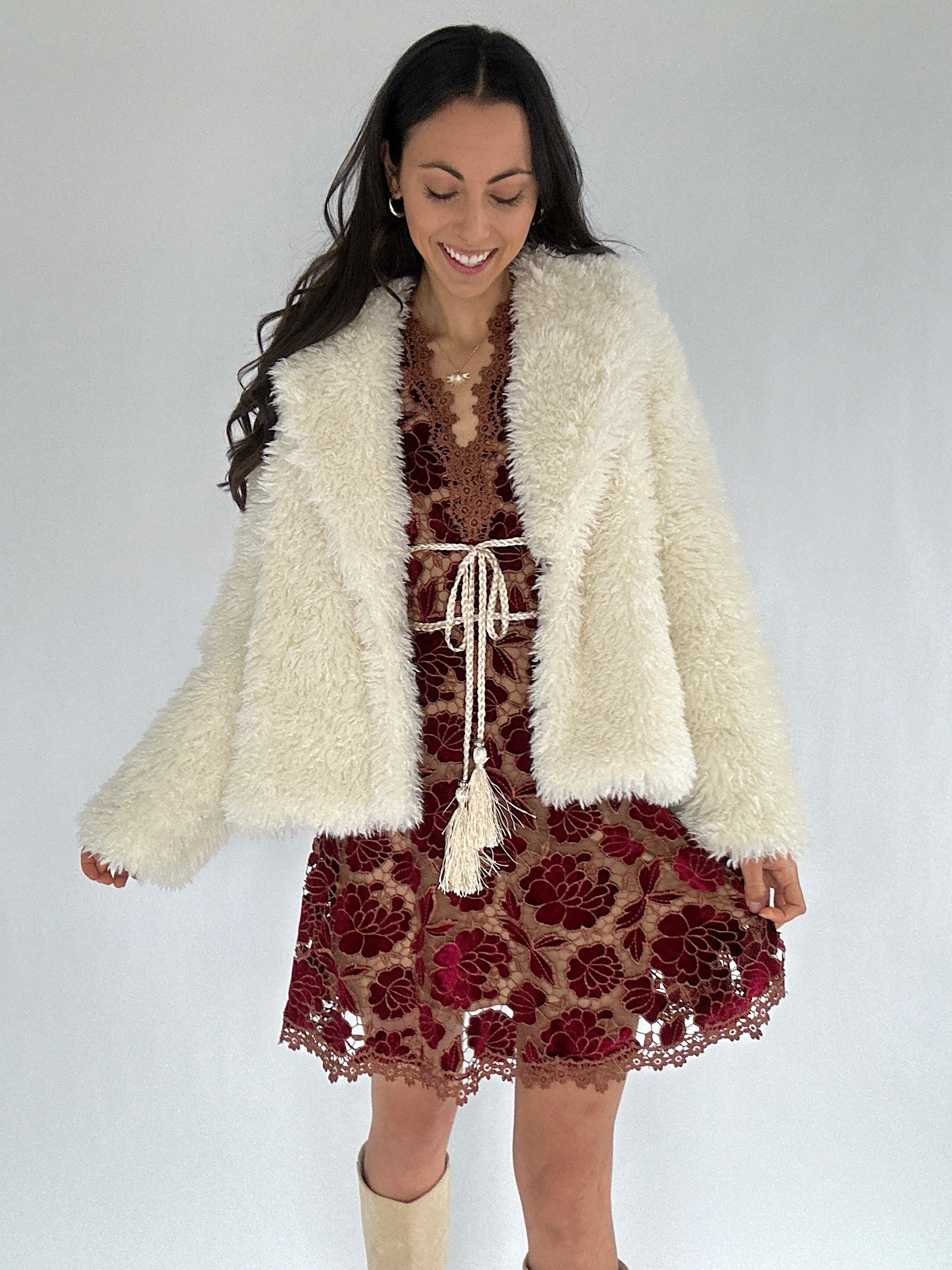 Woman wearing a white fluffy cardigan over a floral dress on a plain background