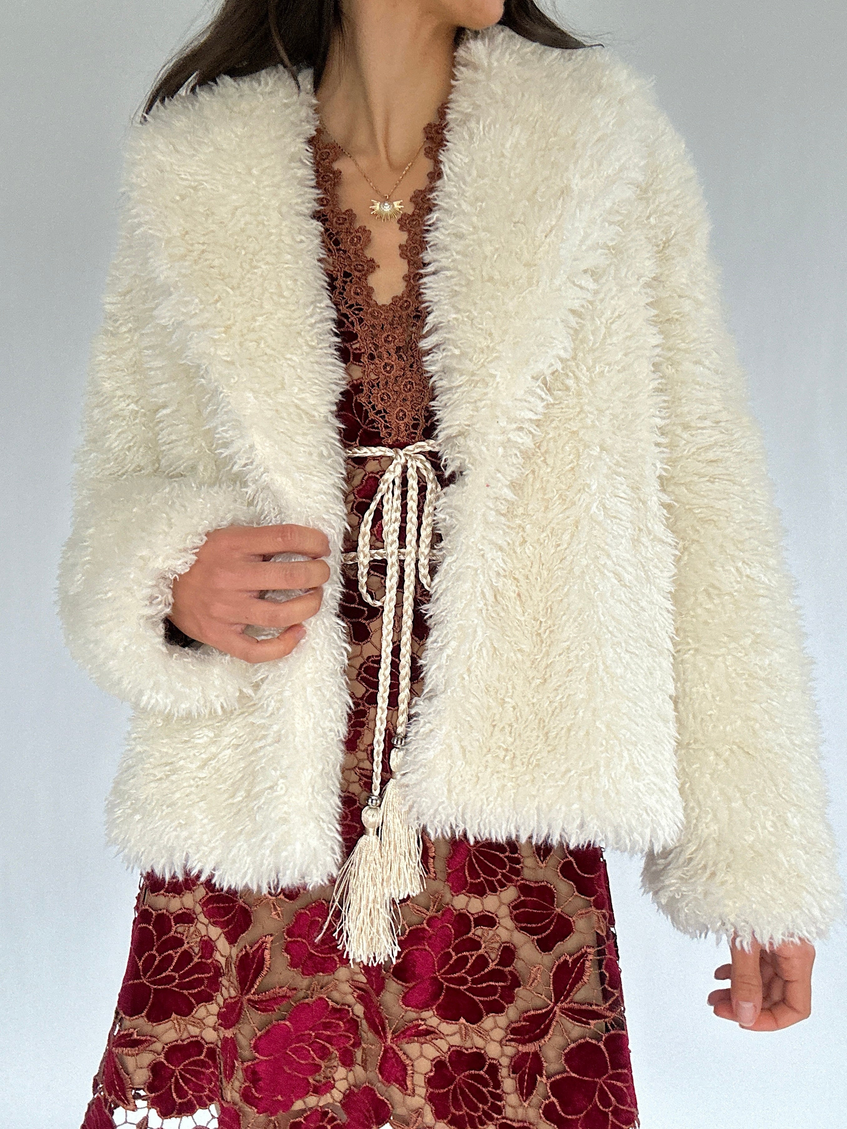 Person wearing a fluffy white jacket over a red patterned dress on a plain background