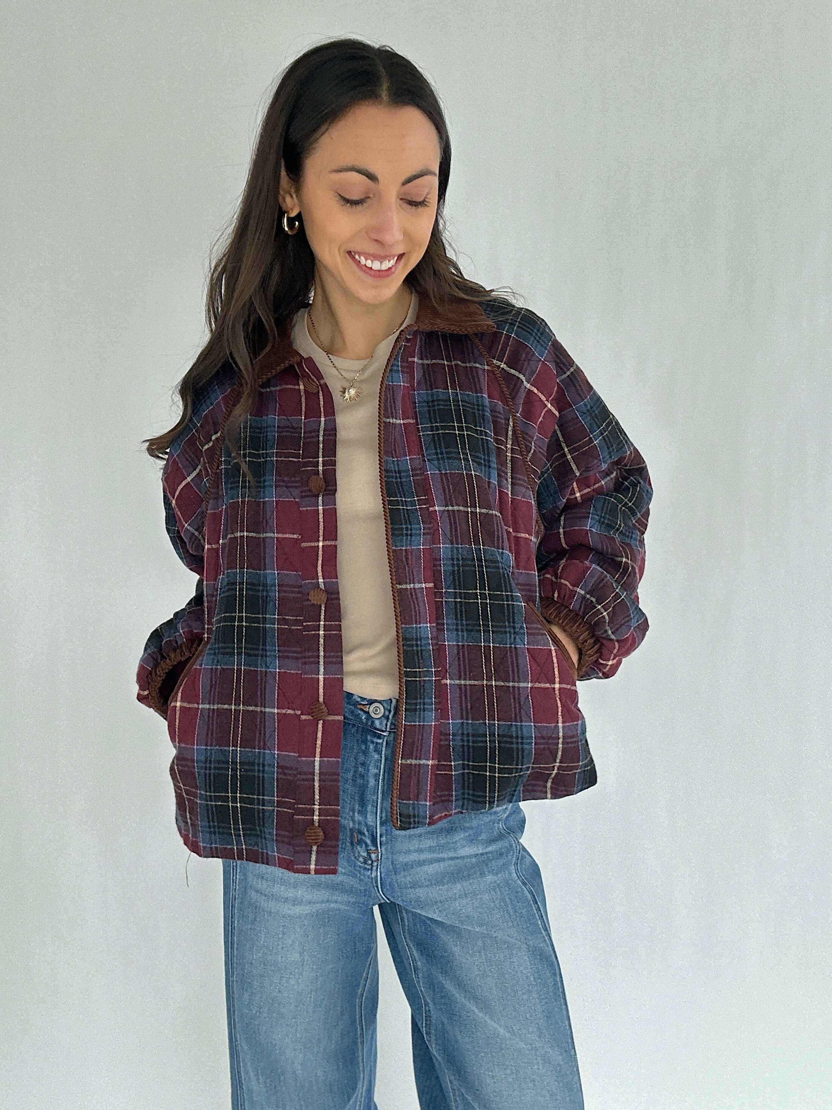 Woman wearing a maroon plaid jacket and jeans on a plain background