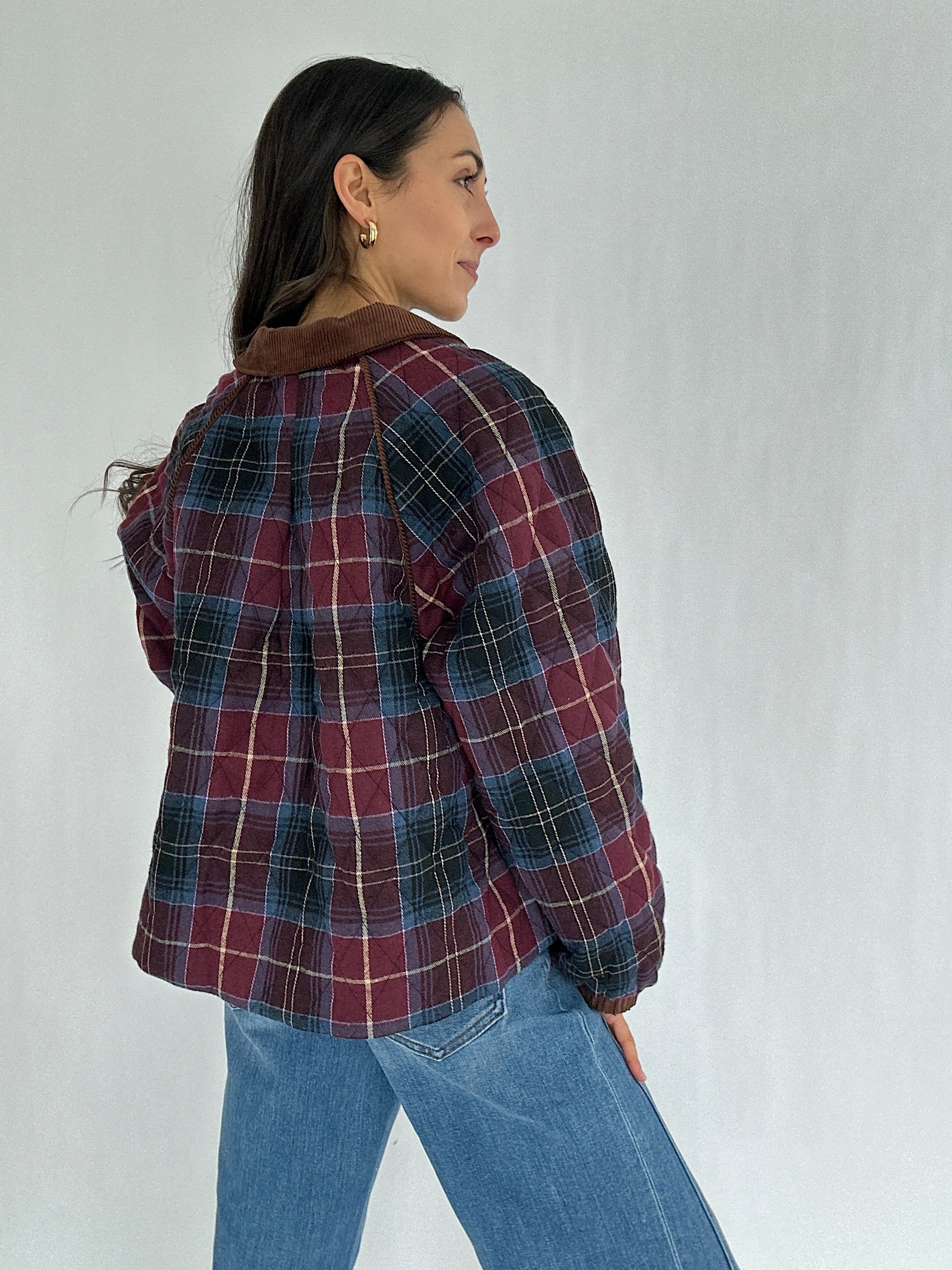 Person wearing a maroon plaid jacket and jeans against a plain background showing the back