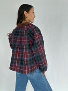 Person wearing a maroon plaid jacket and jeans against a plain background showing the back