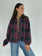 Woman wearing a maroon plaid jacket and jeans against a plain background