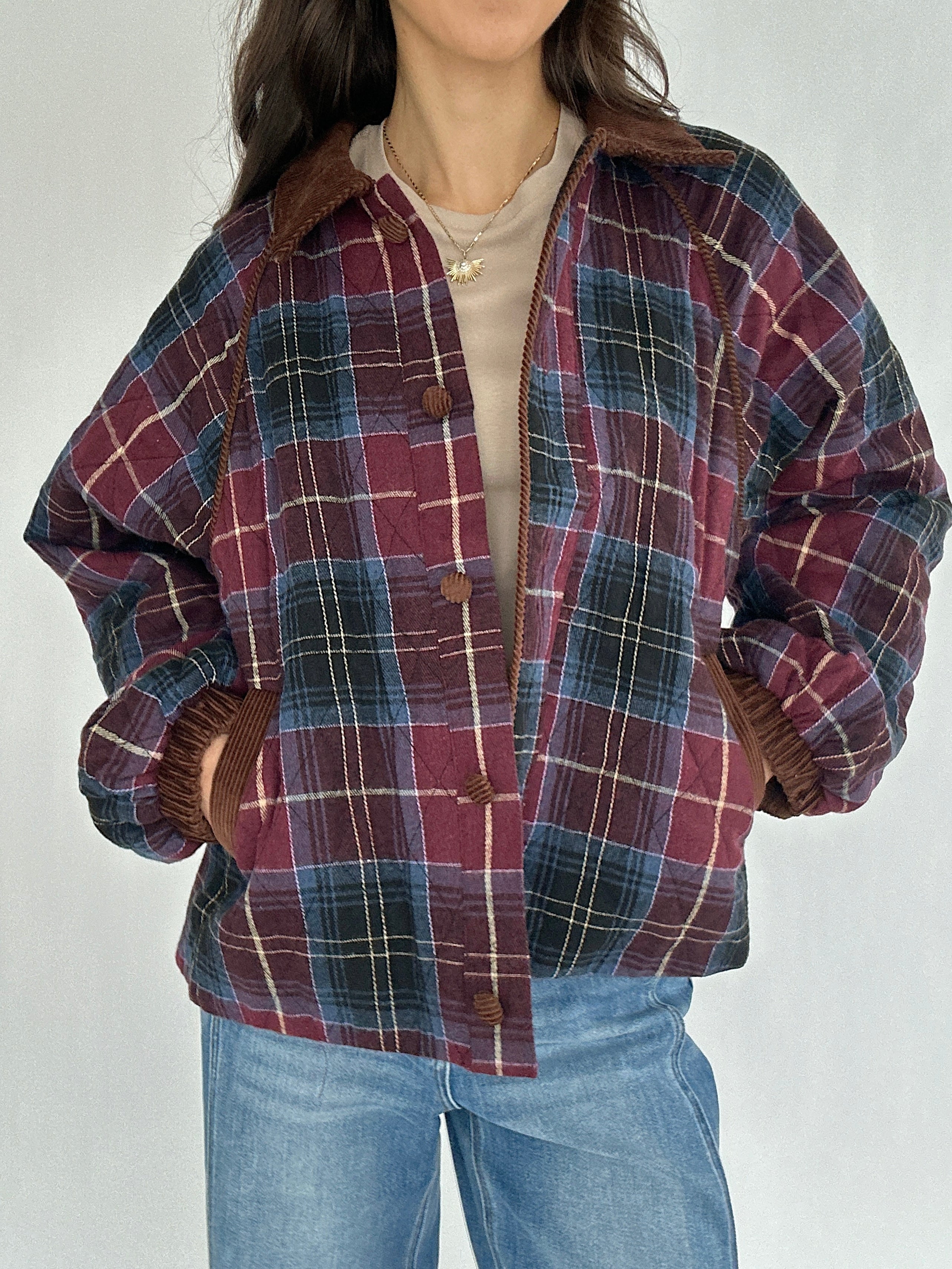 Person wearing a maroon plaid jacket with hands in pockets against a neutral background