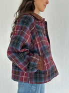 Person wearing a plaid jacket with corduroy accents on a plain background showing hands in side pockets