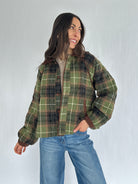 Person wearing a green plaid jacket and blue jeans against a white background