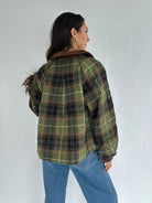 Person wearing a green plaid jacket and blue jeans against a white background showing back