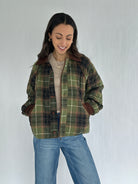 Woman wearing a green plaid jacket and jeans against a plain background with hands in pockets