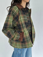 Green plaid jacket with brown accents worn by a person on a white background with hands in pockets