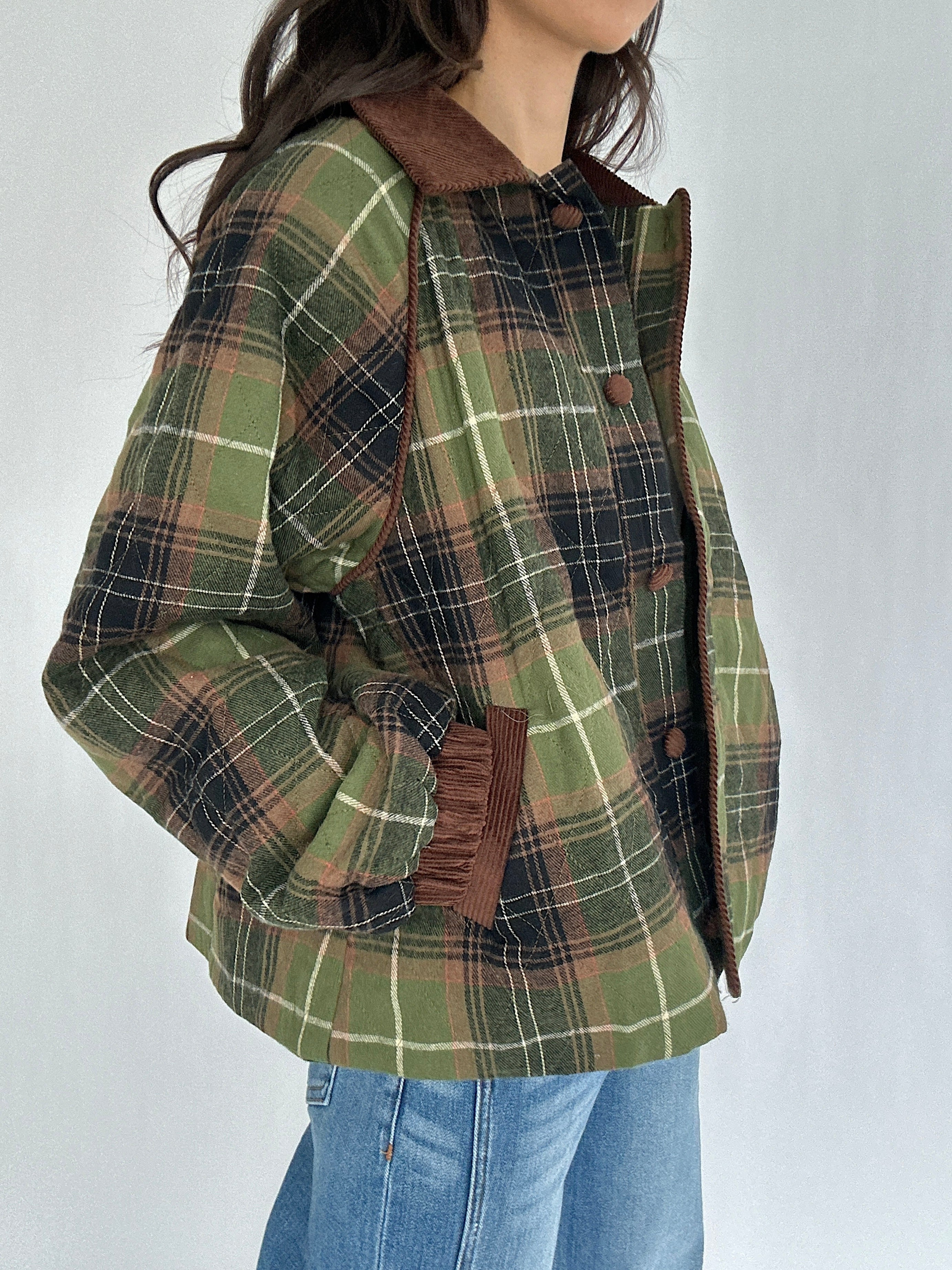 Green plaid jacket with brown accents worn by a person on a white background with hands in pockets