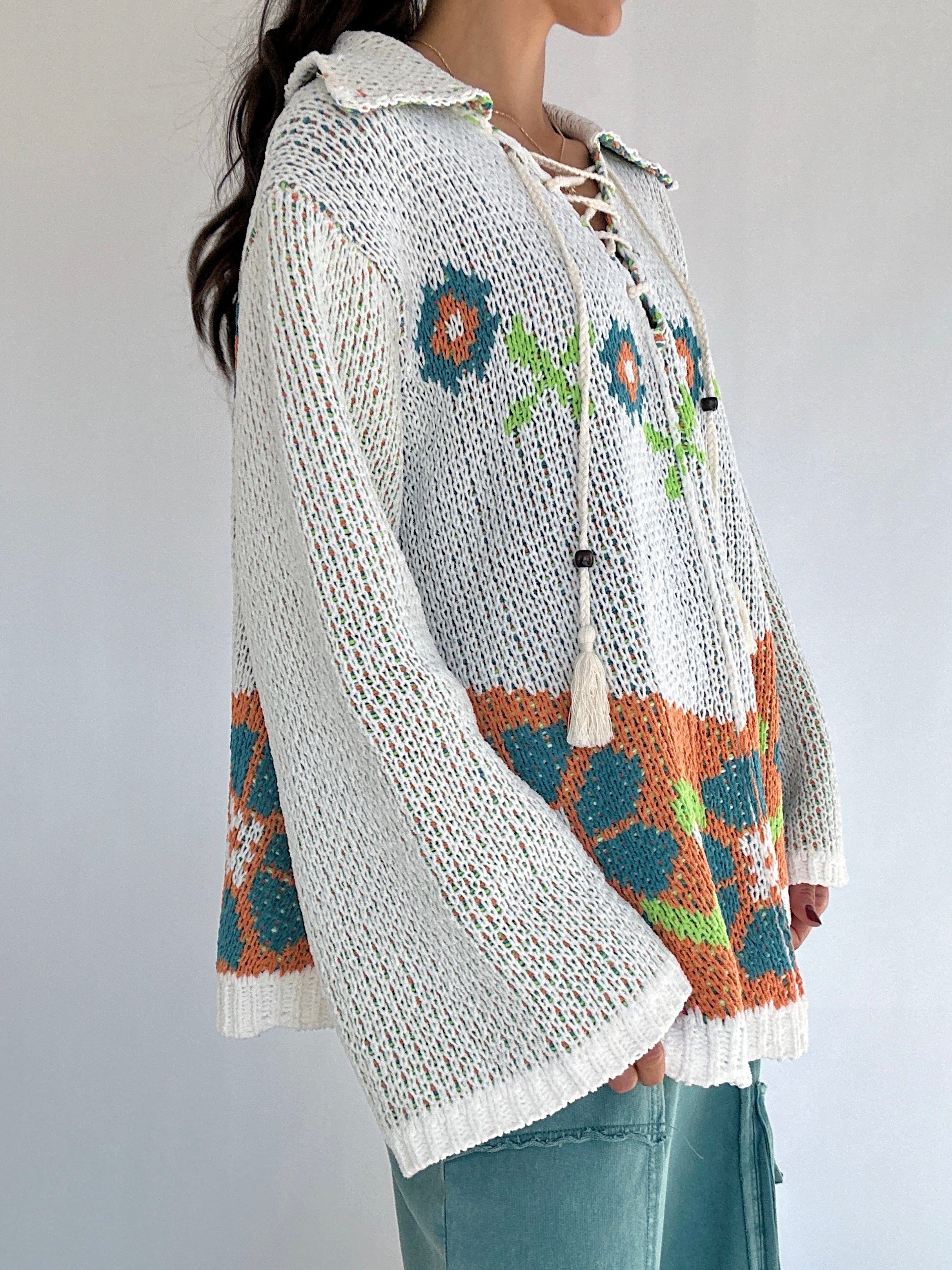 Person wearing a knitted chenille sweater with floral patterns on a plain background showing side