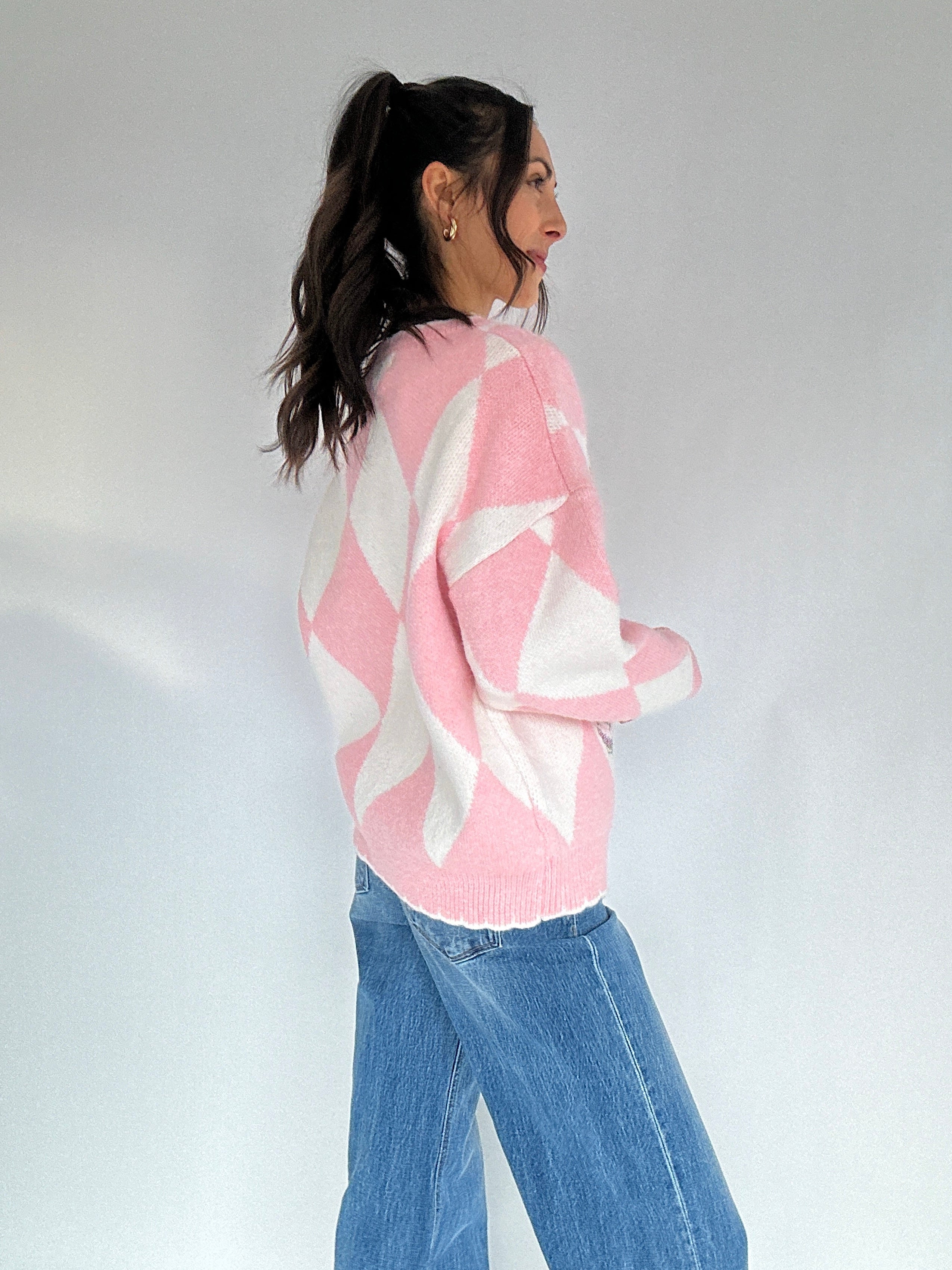 Person wearing a pink and white patterned sweater with blue jeans against a plain background