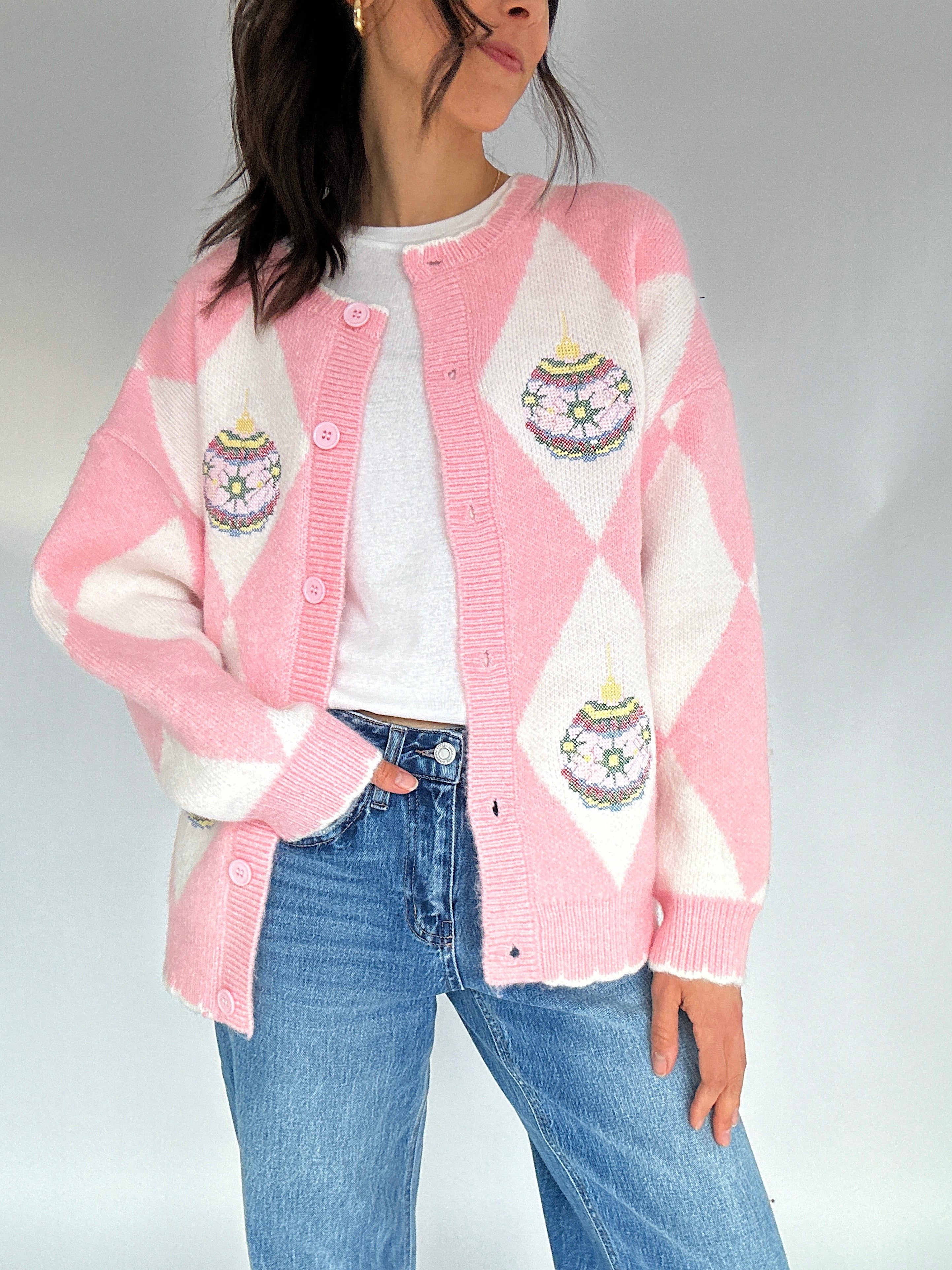 Person wearing a pink and white argyle cardigan with embroidered ornament designs on a plain background