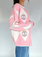 Person wearing a pink and white argyle cardigan with ornament designs on a plain background from side