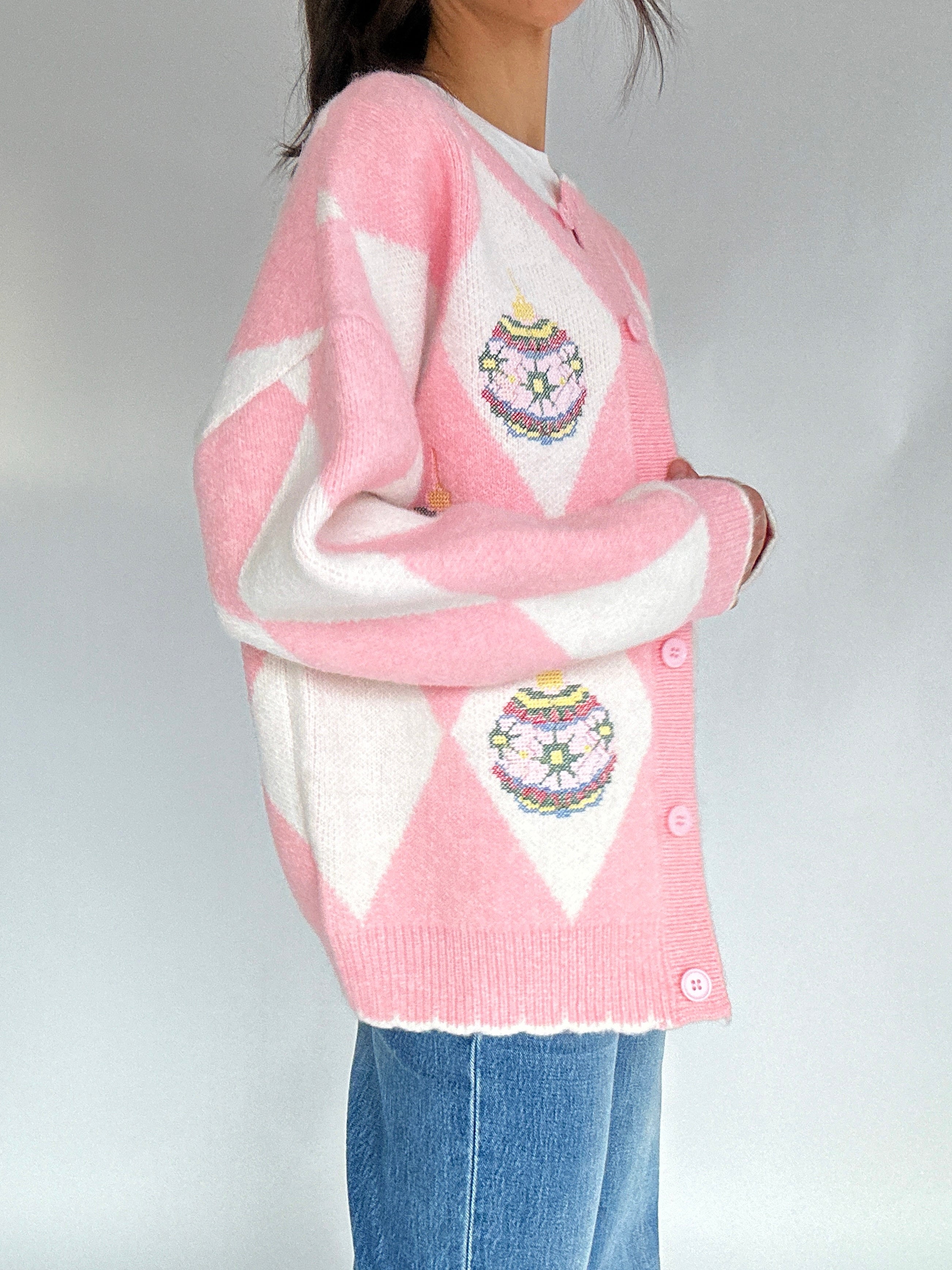Person wearing a pink and white argyle cardigan with ornament designs on a plain background from side