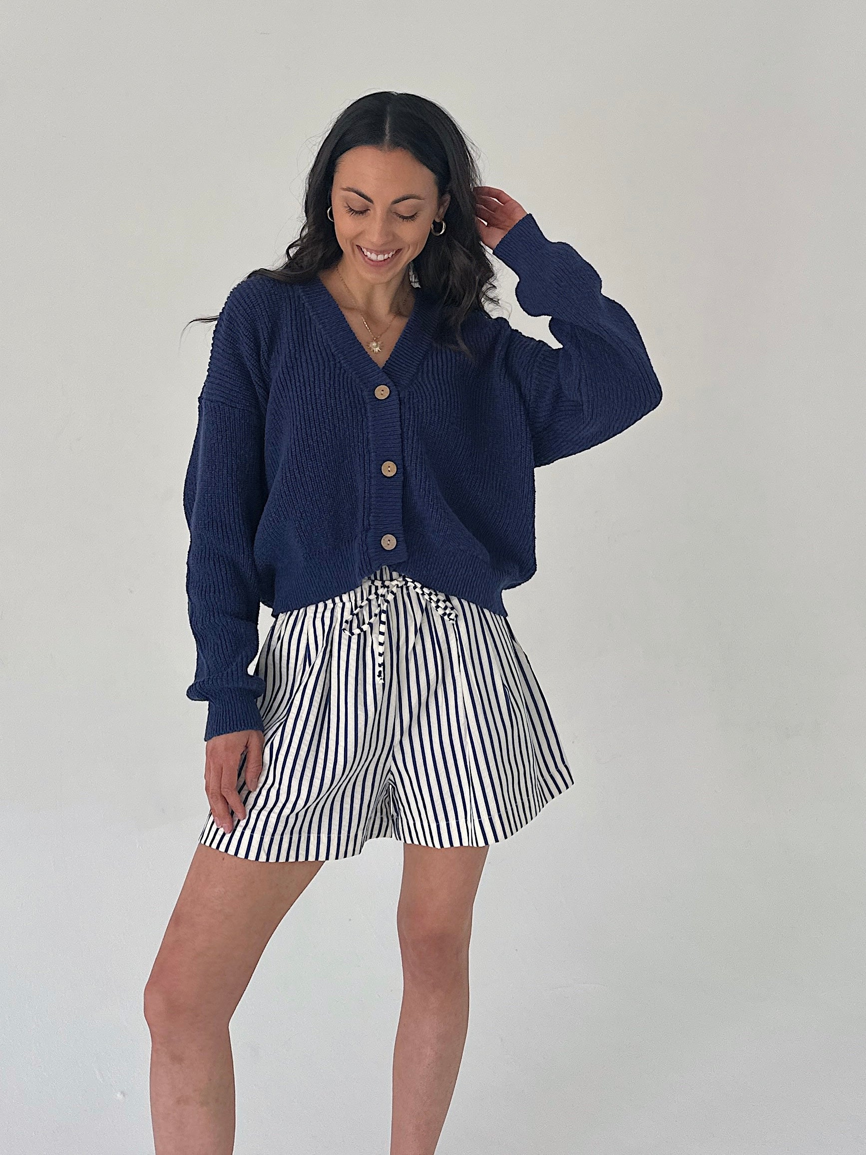 Woman wearing a navy cardigan and striped shorts against a white background