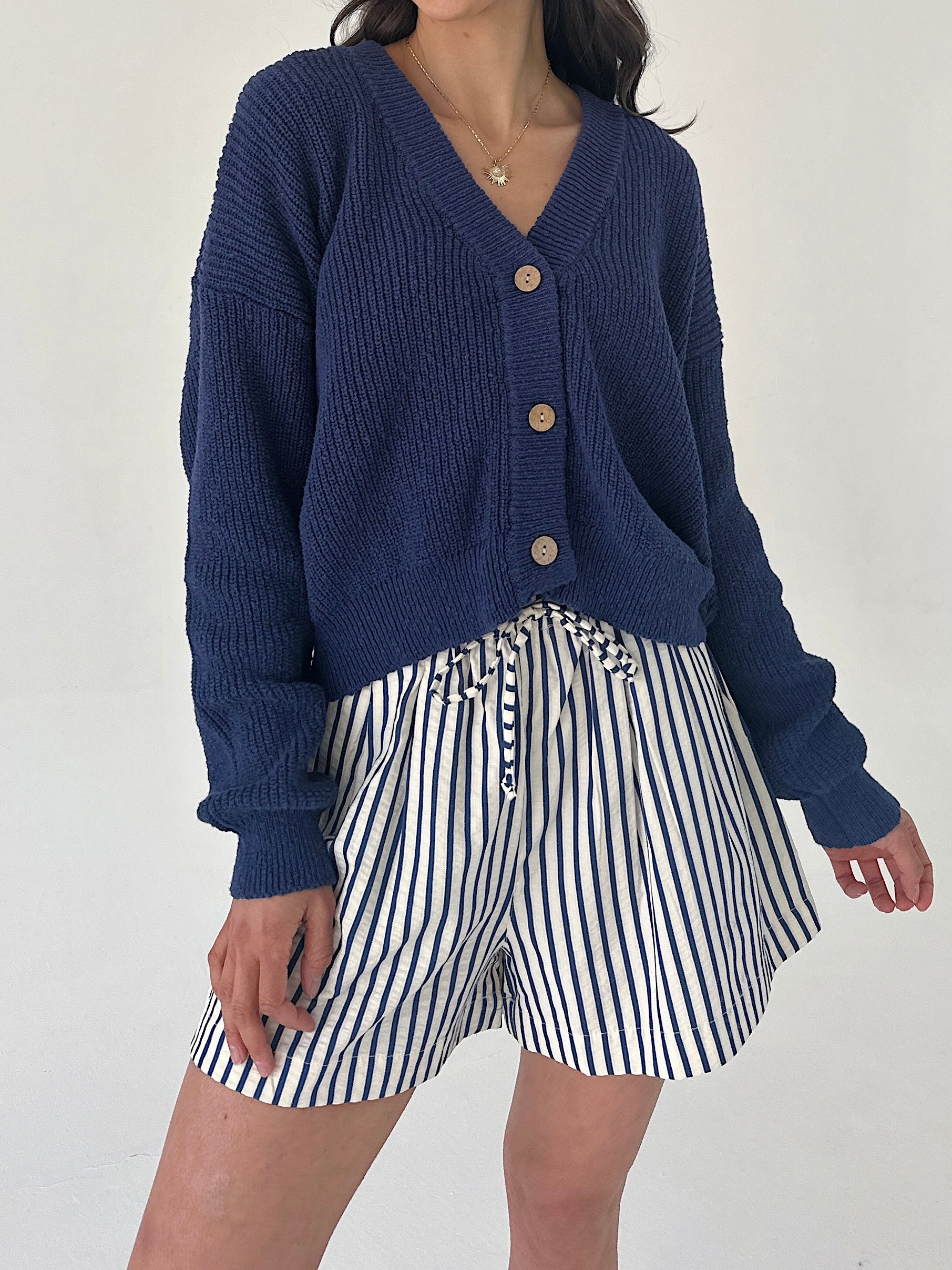 Person wearing a blue cardigan and striped shorts on a white background