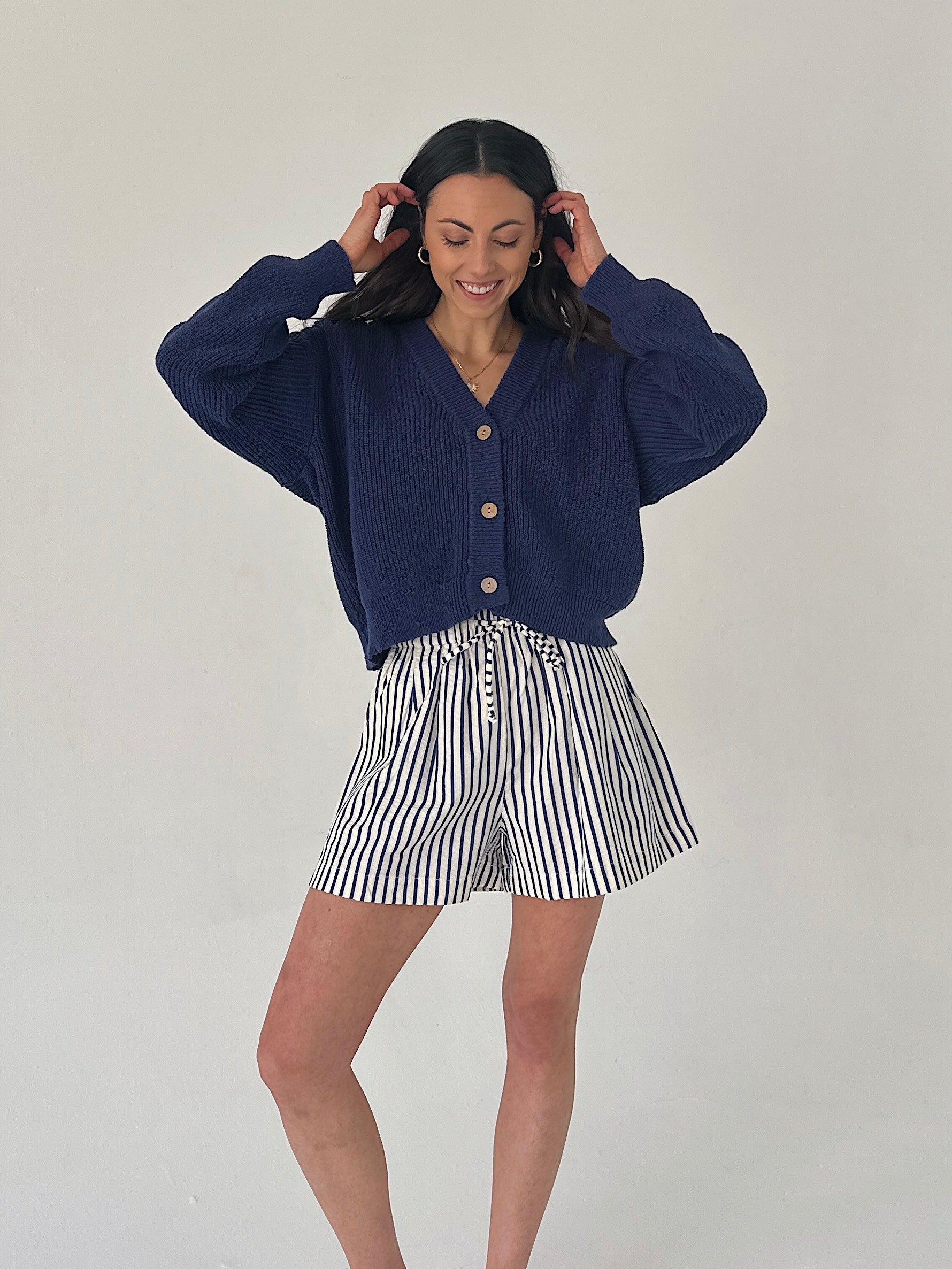 Woman wearing a navy blue cardigan and striped shorts on a plain background