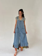 Woman wearing a denim overalls with ruffled hem on a plain background