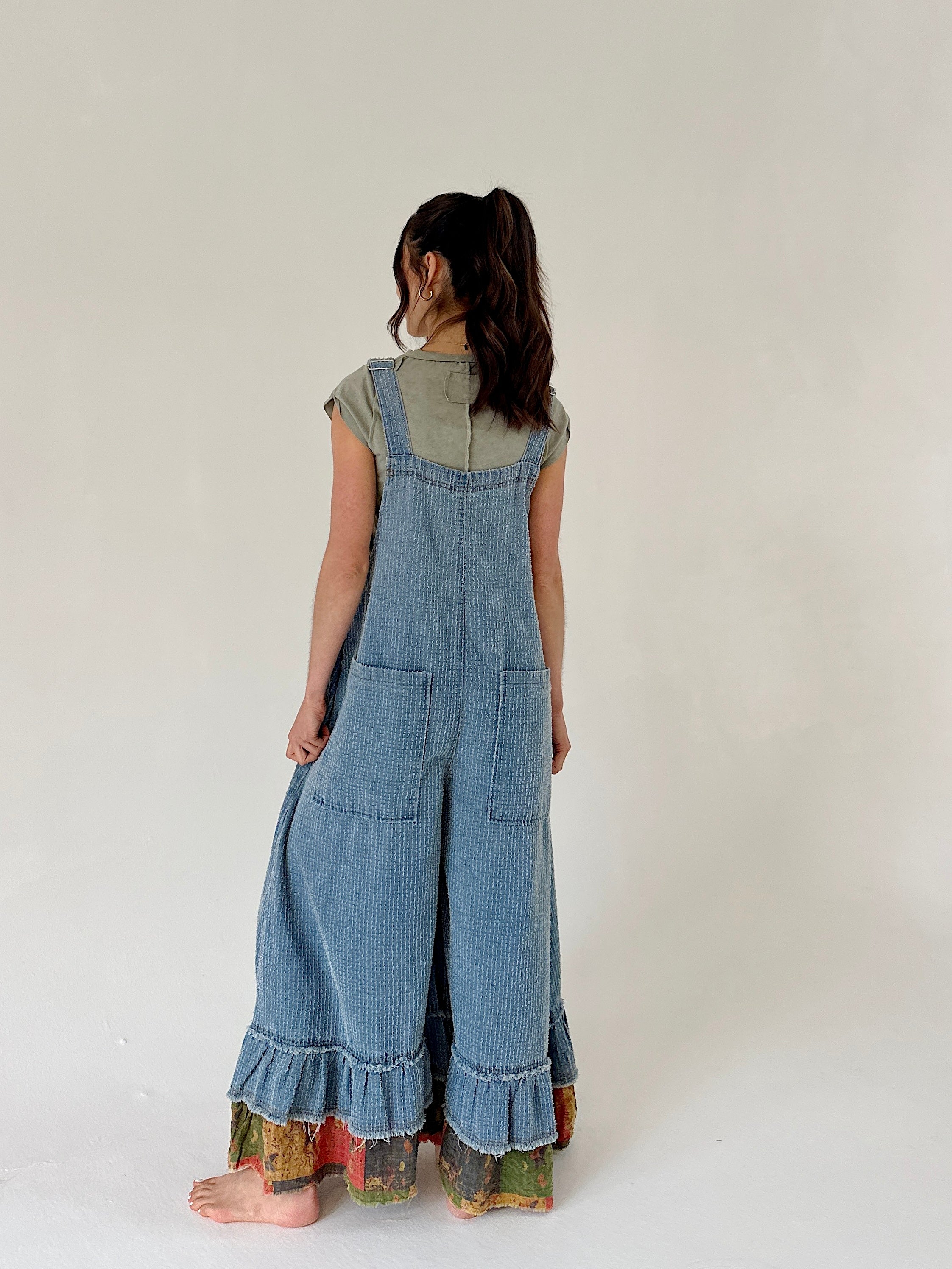 Person wearing a denim overalls  from the back with a plain background