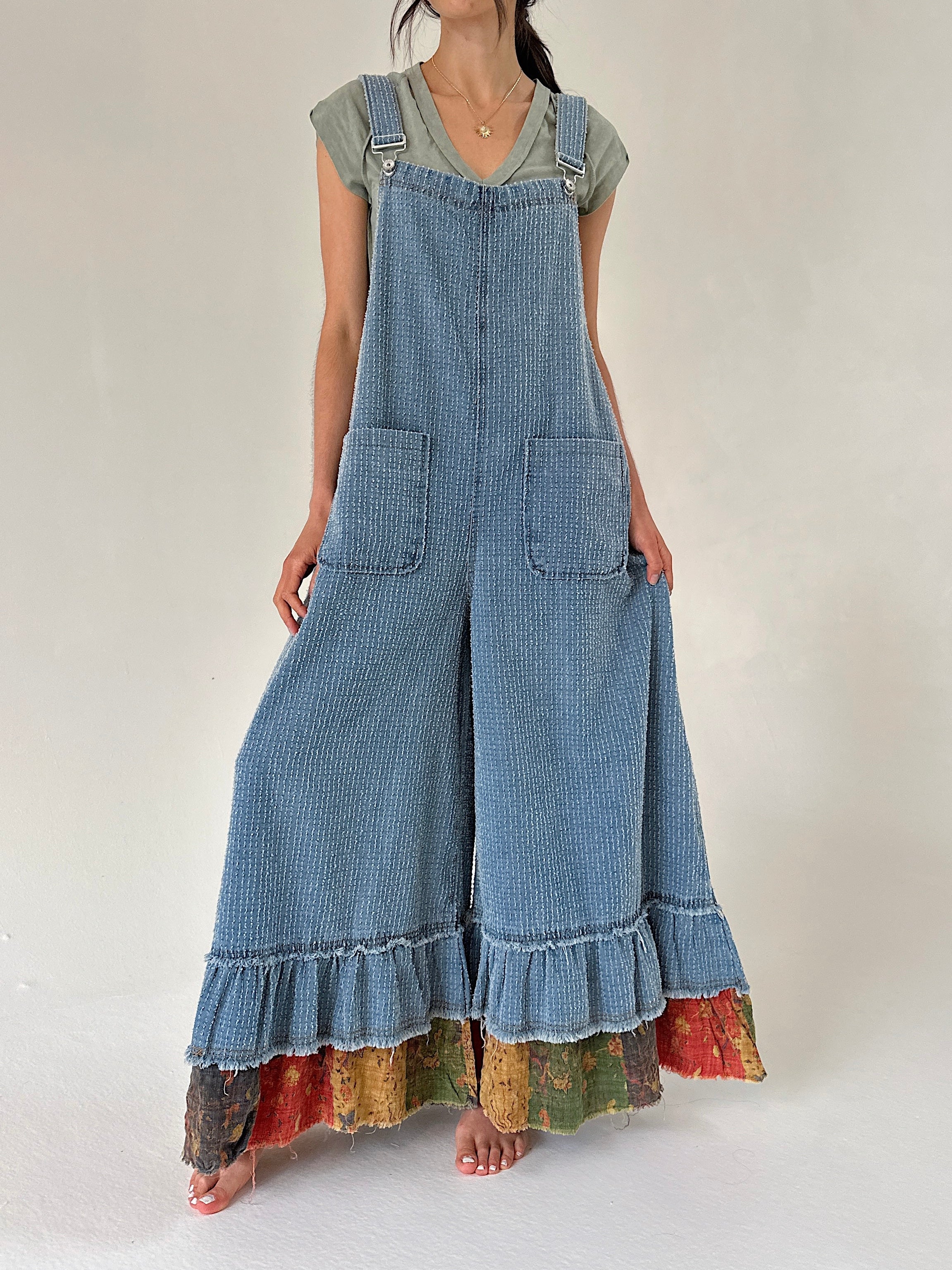 Person wearing a long denim overalls with ruffled bottom on a plain background