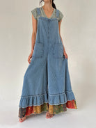 Person wearing a long denim overalls with ruffled bottom on a plain background