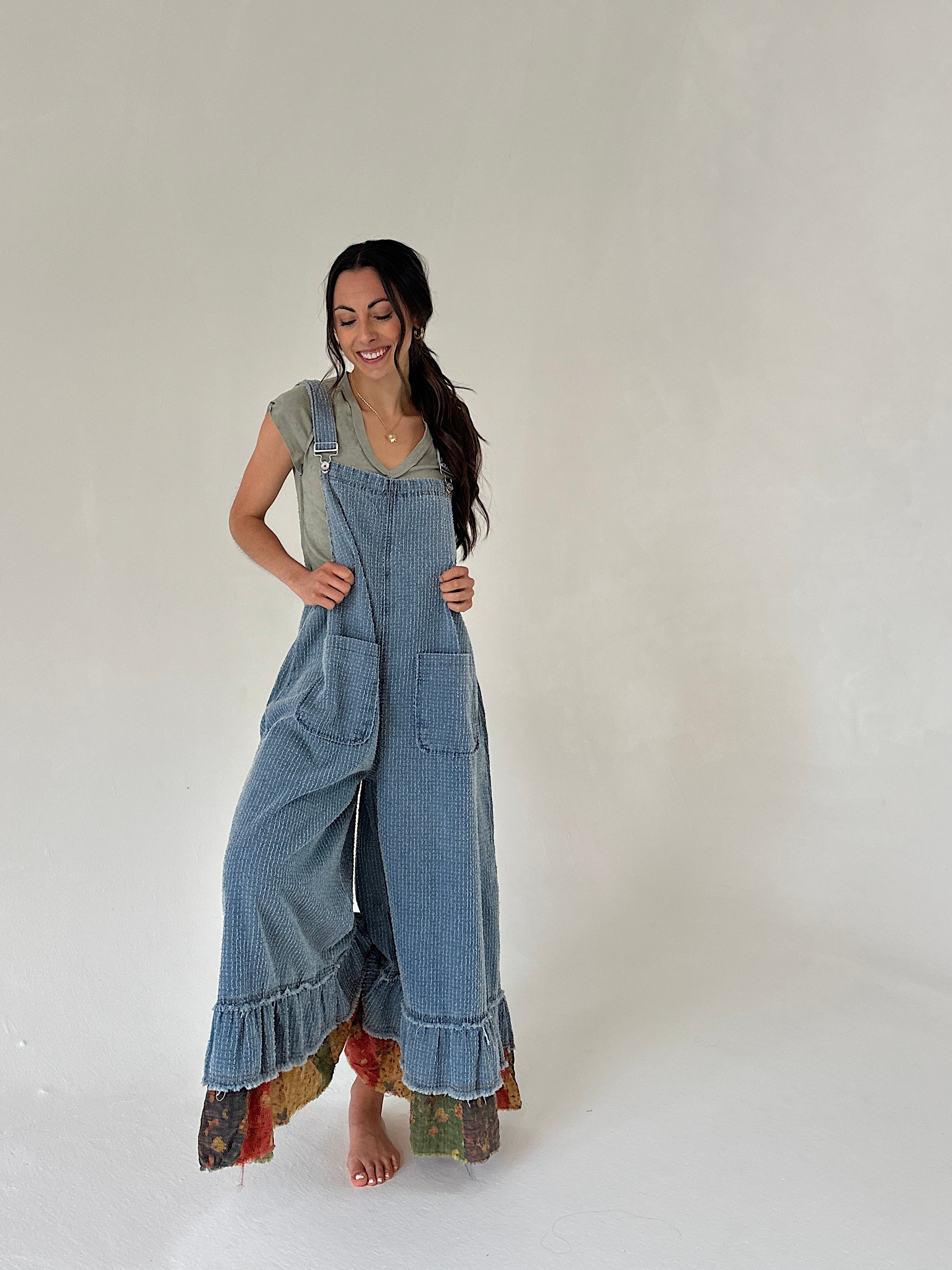 Woman wearing denim overalls with ruffled hem on a plain background