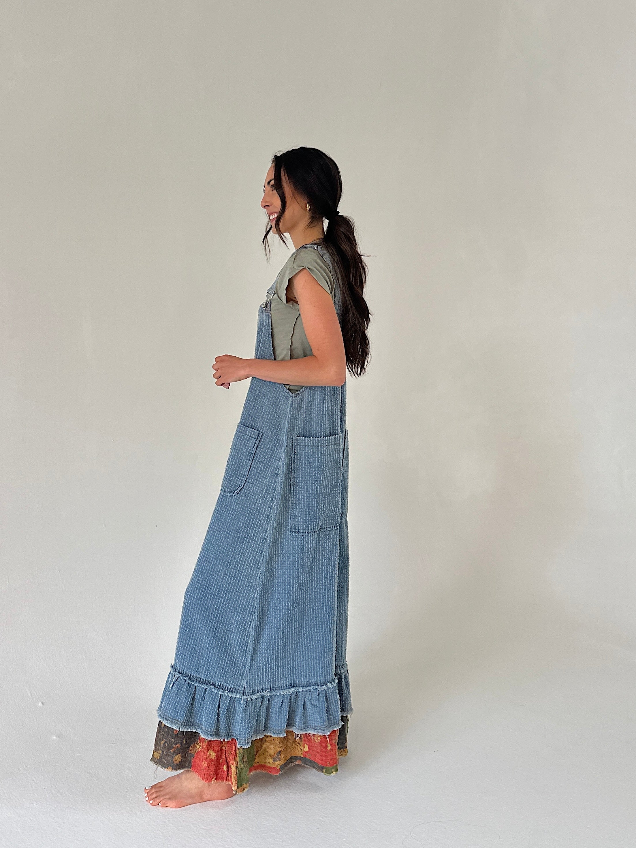 Woman denim overalls with a wide leg fit and ruffle hem from side with a plain background